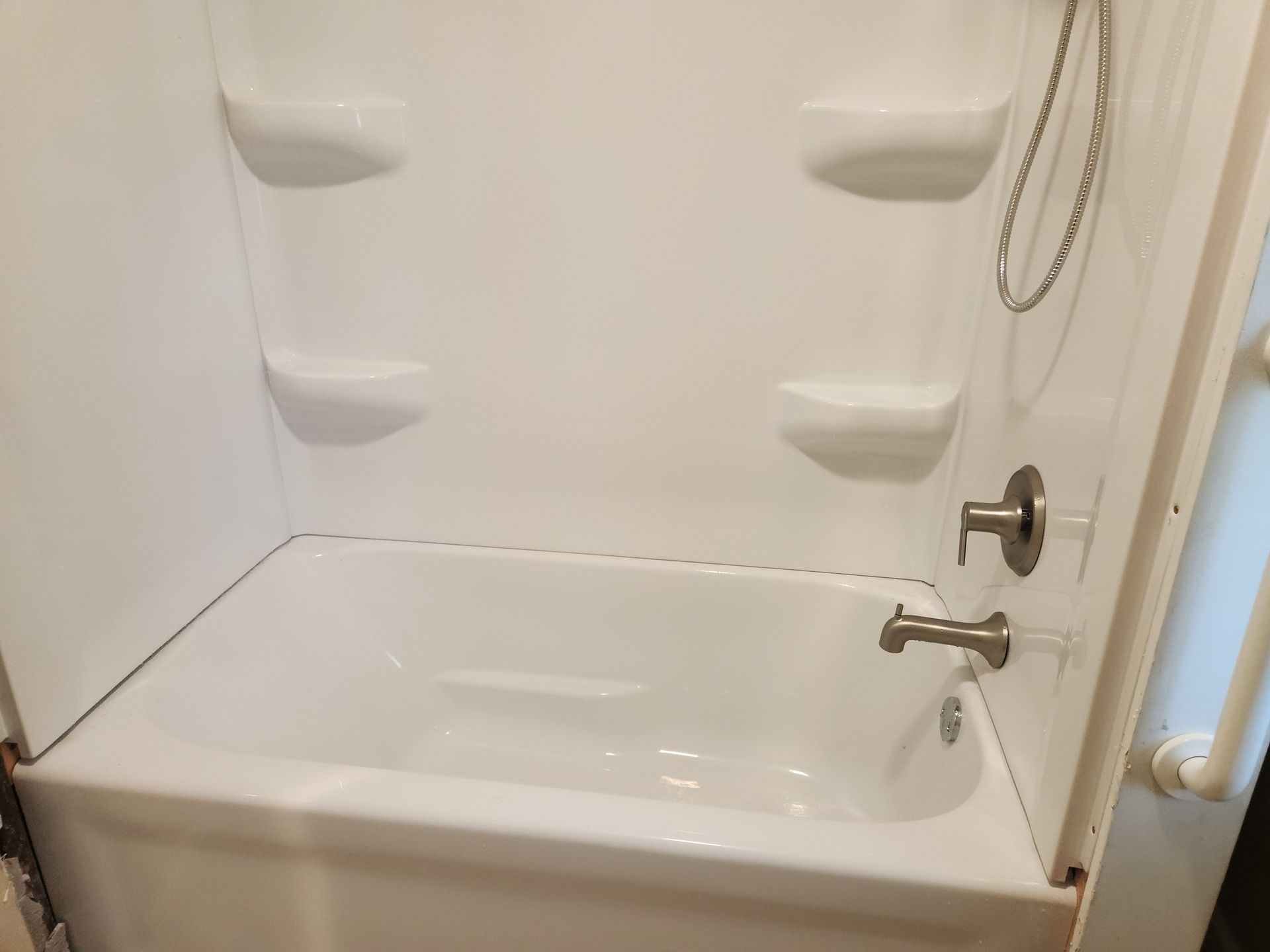 White bathtub and shower stall with grab bar and chrome faucet in a bathroom.
