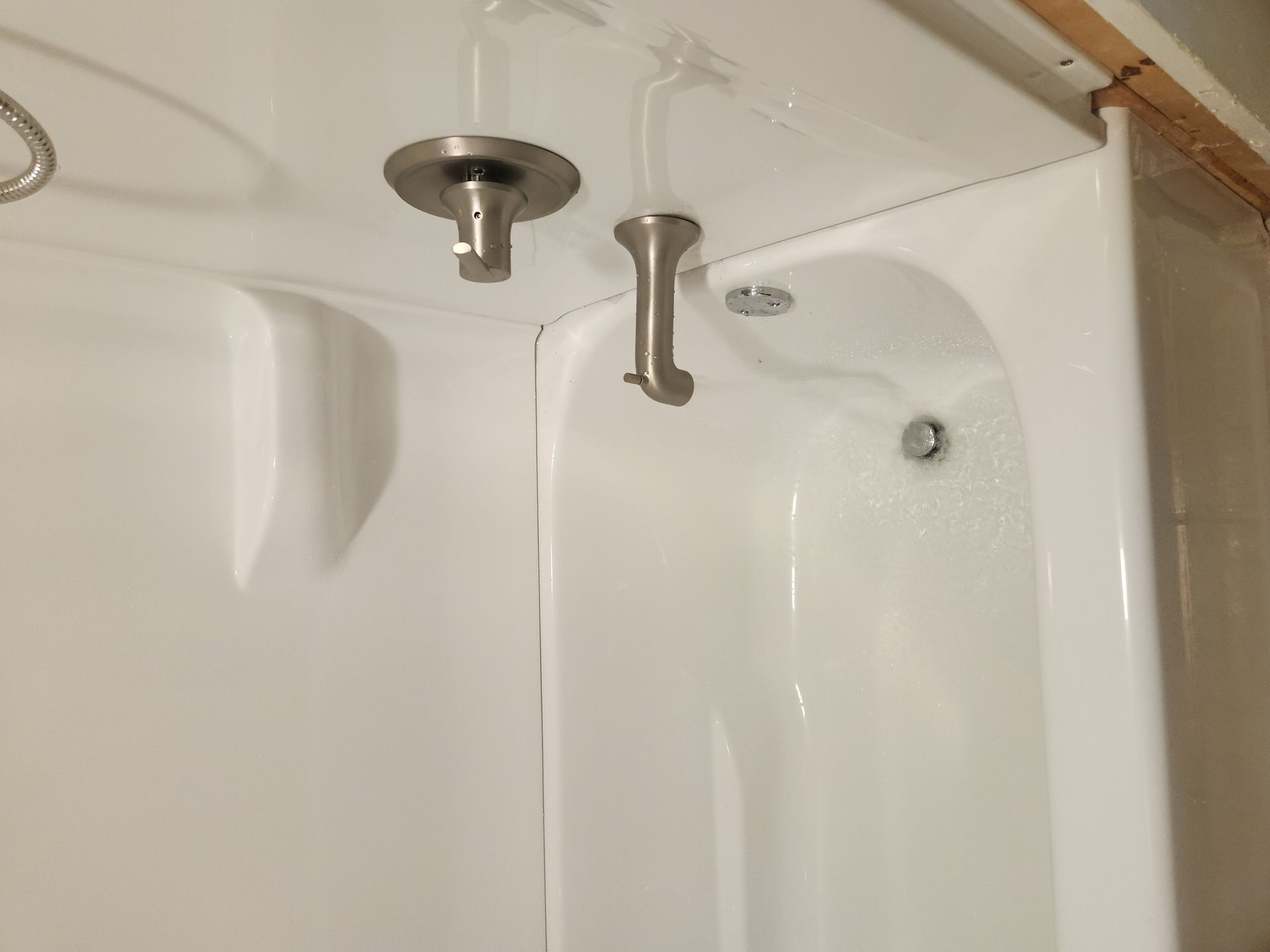 White shower/tub corner with chrome showerhead and faucet under beige tile wall