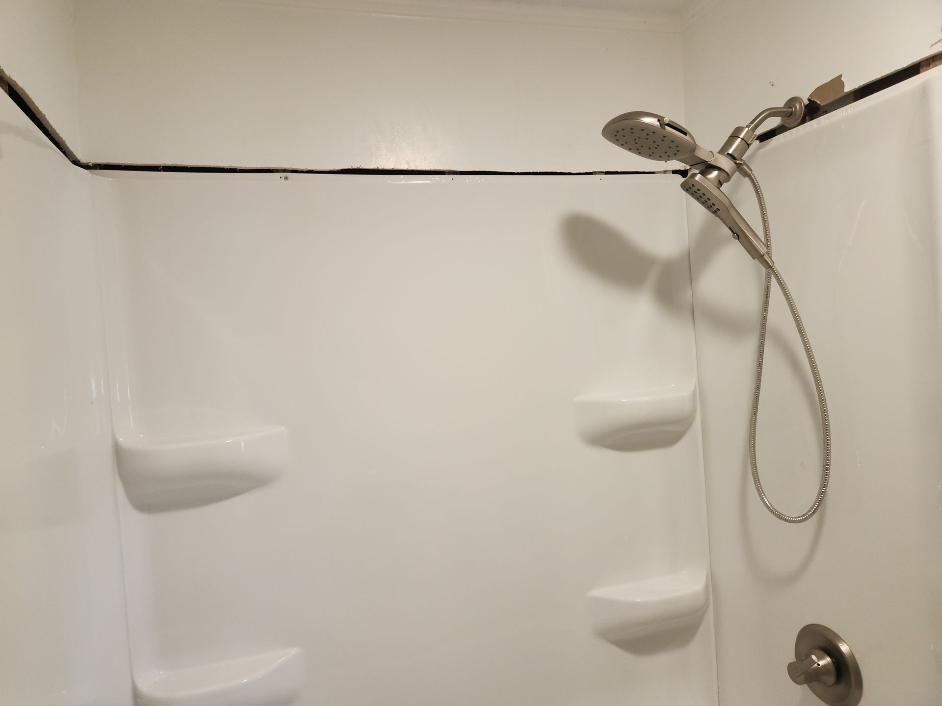 White shower stall with built-in shelves and a handheld showerhead on the right.