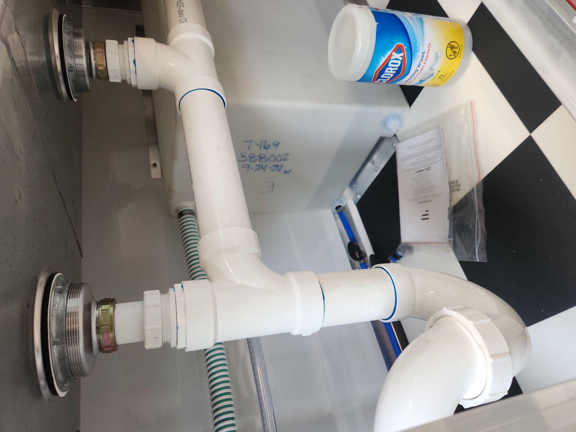 Under-sink plumbing with white PVC pipes, a drain trap, and a small blue-and-yellow container on the right
