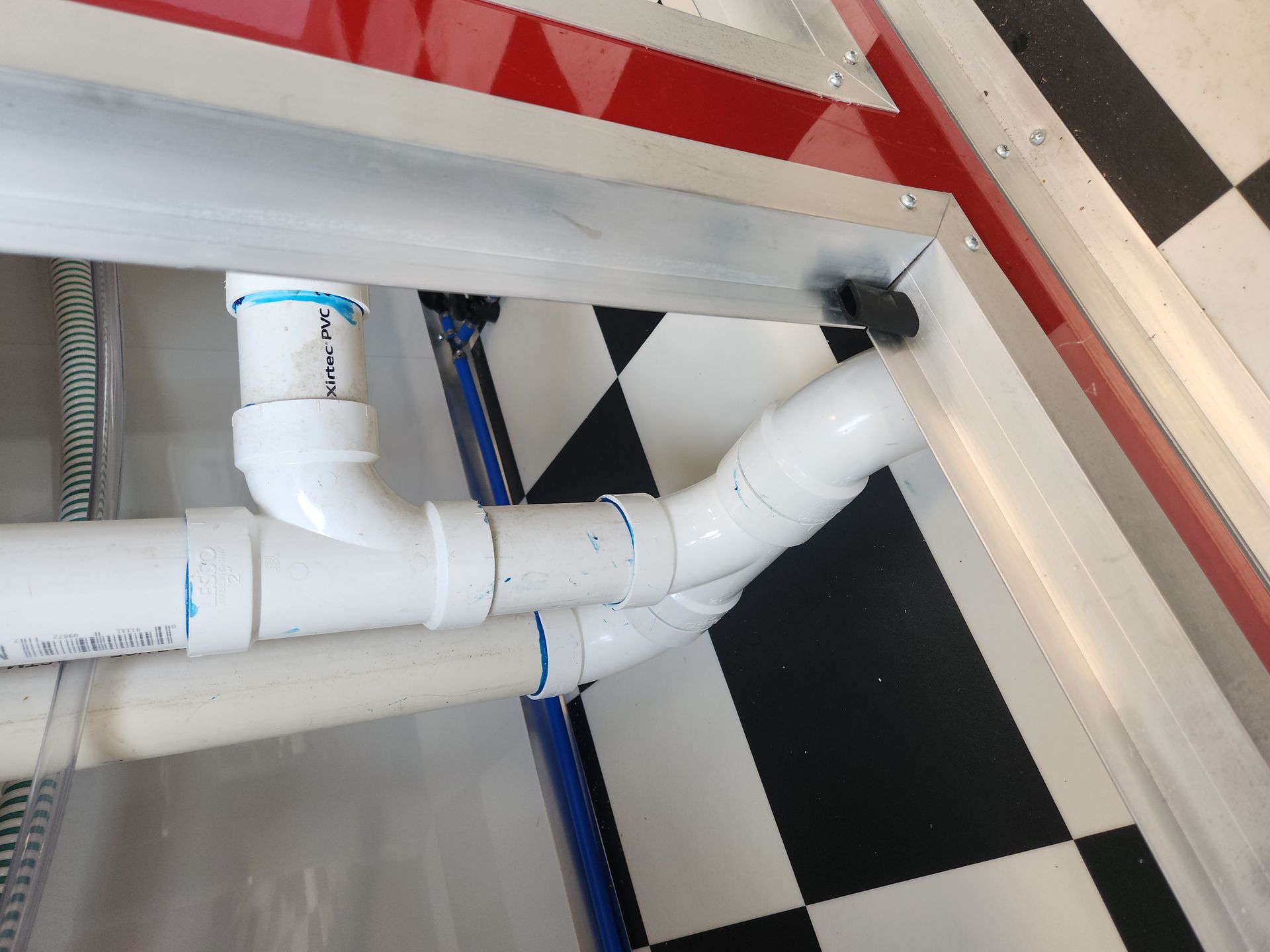 White PVC pipes under a counter beside a red-and-black checkered floor and wall trim