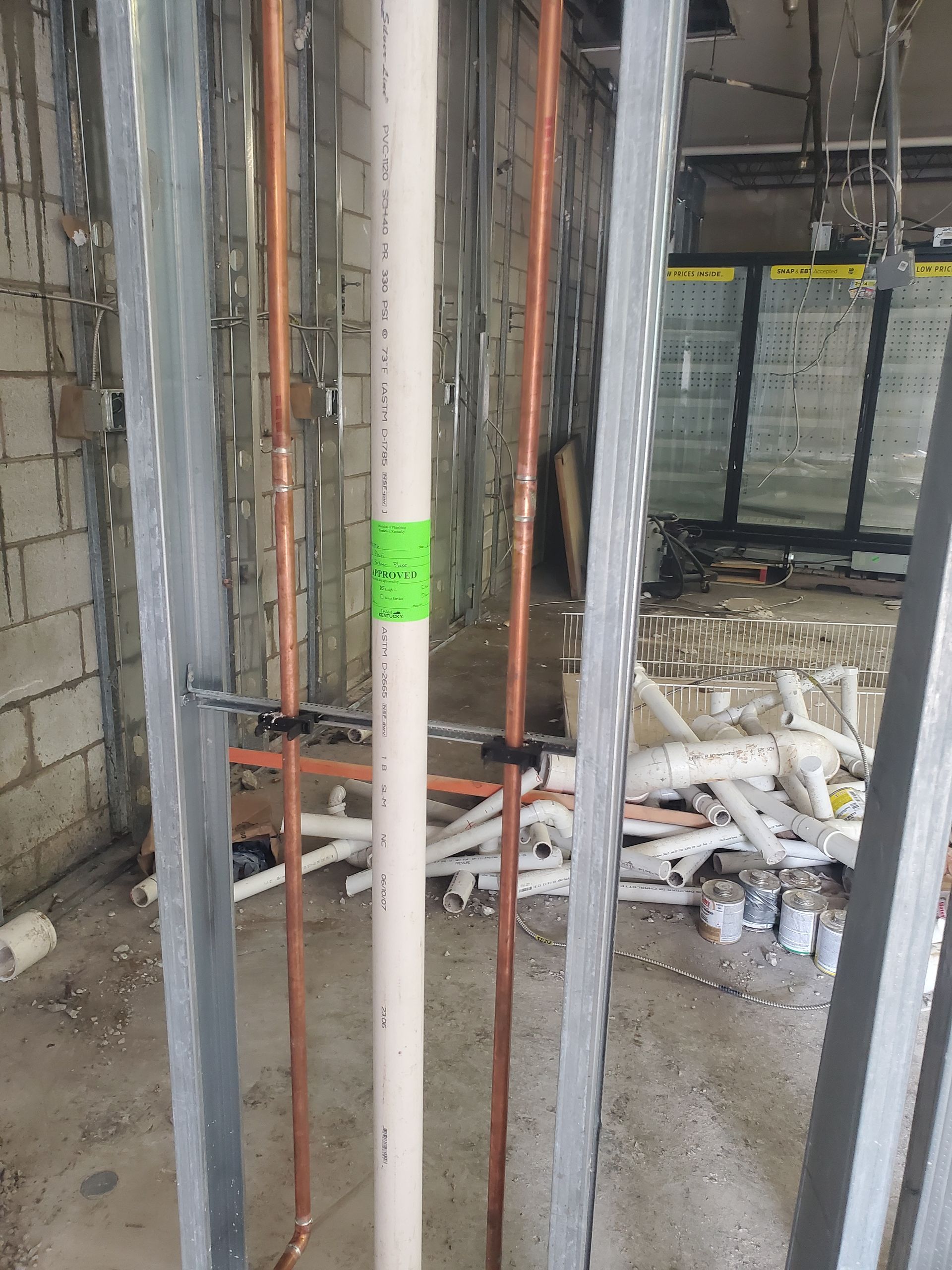 Construction site with exposed pipes and debris beside a concrete wall and doorway.