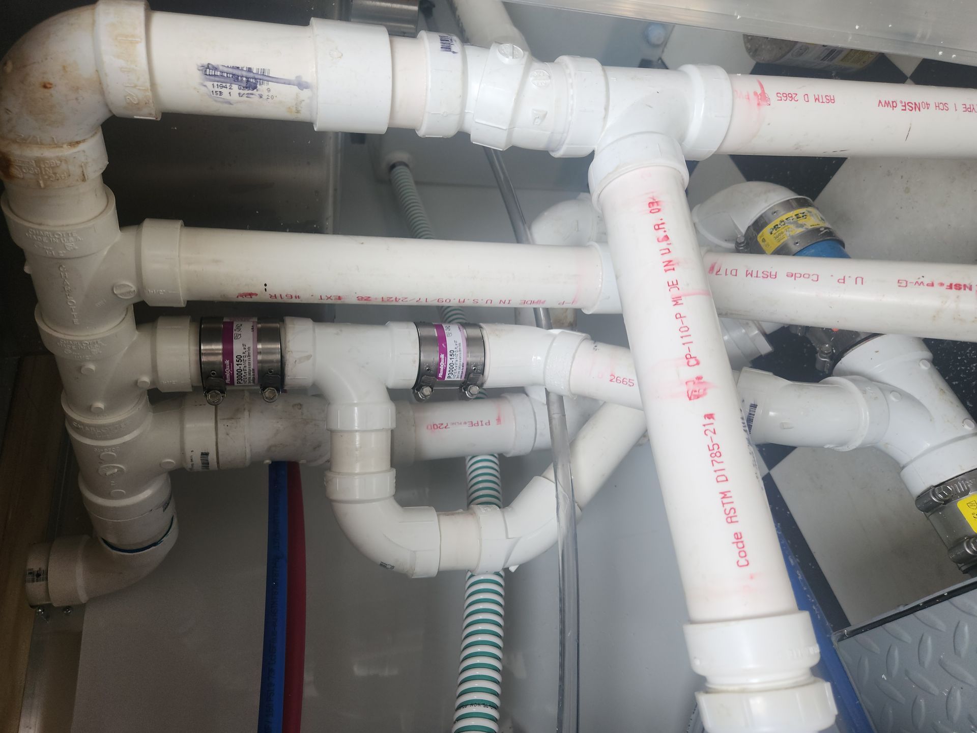 White PVC pipes and joints in a utility space, with red and blue marked lines and insulated sections.