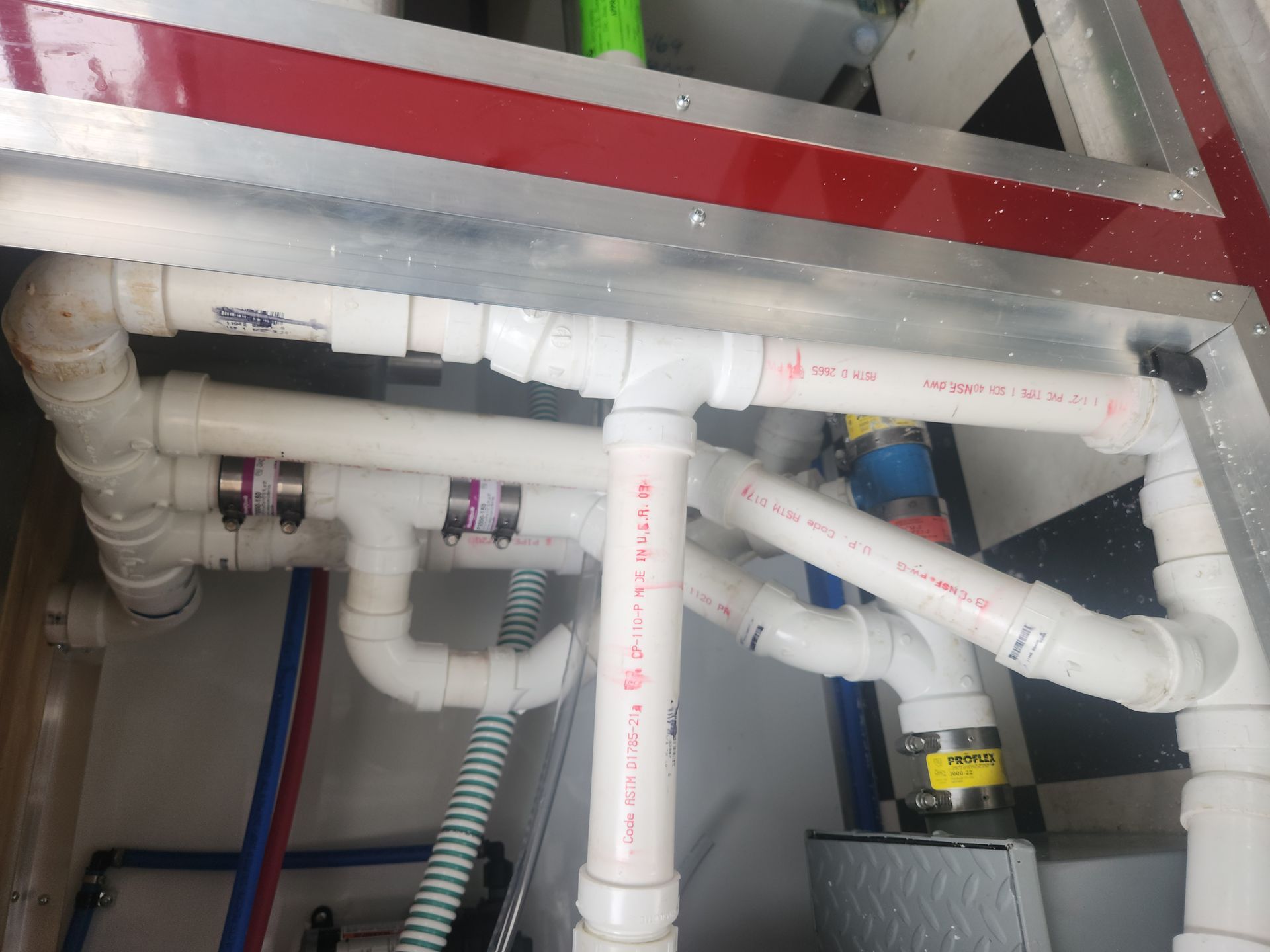 Exposed white PVC pipes and fittings under a ceiling, with red and blue utility lines in a utility space