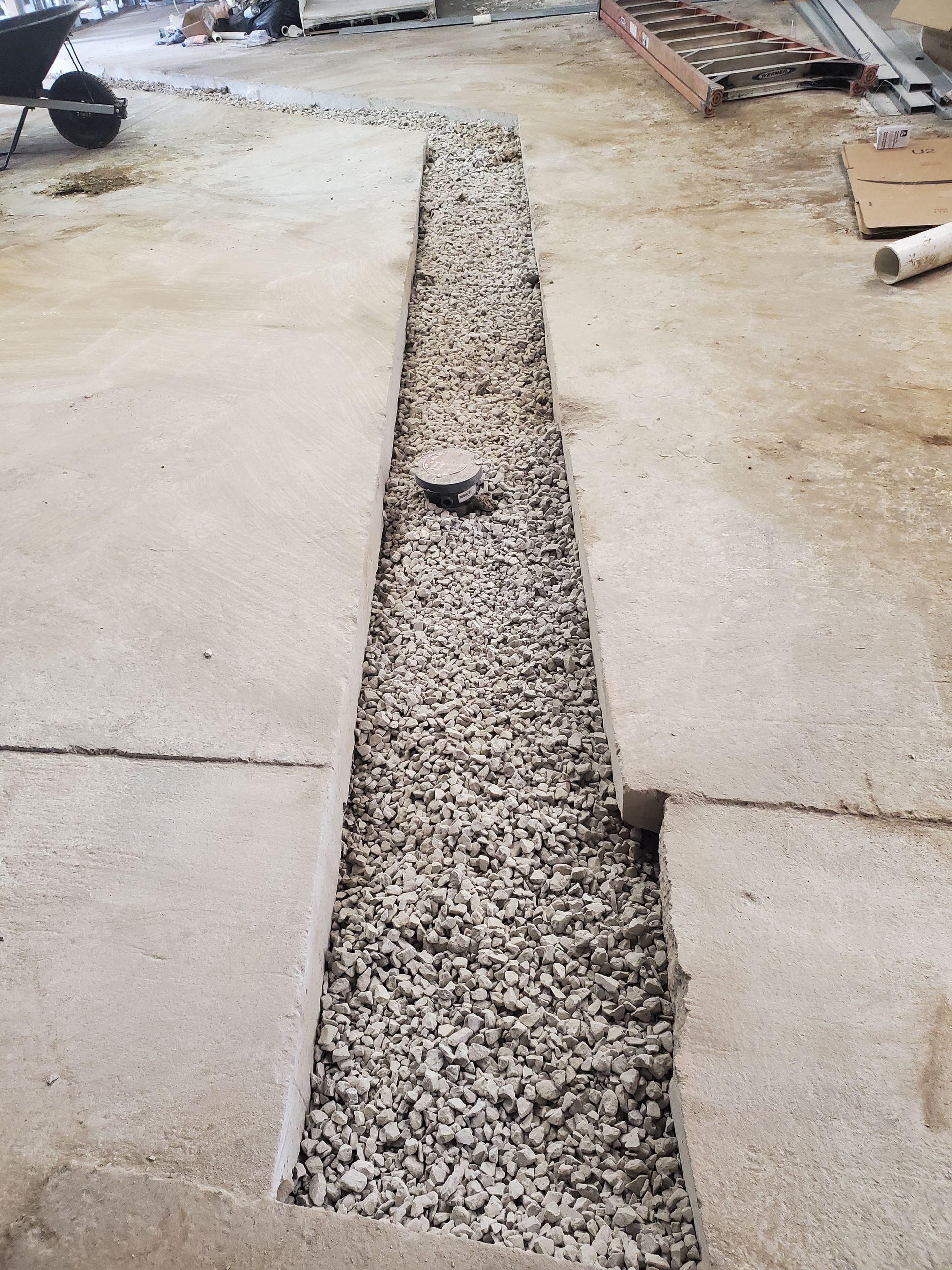 Gravel-filled trench between broken concrete slabs on a construction site