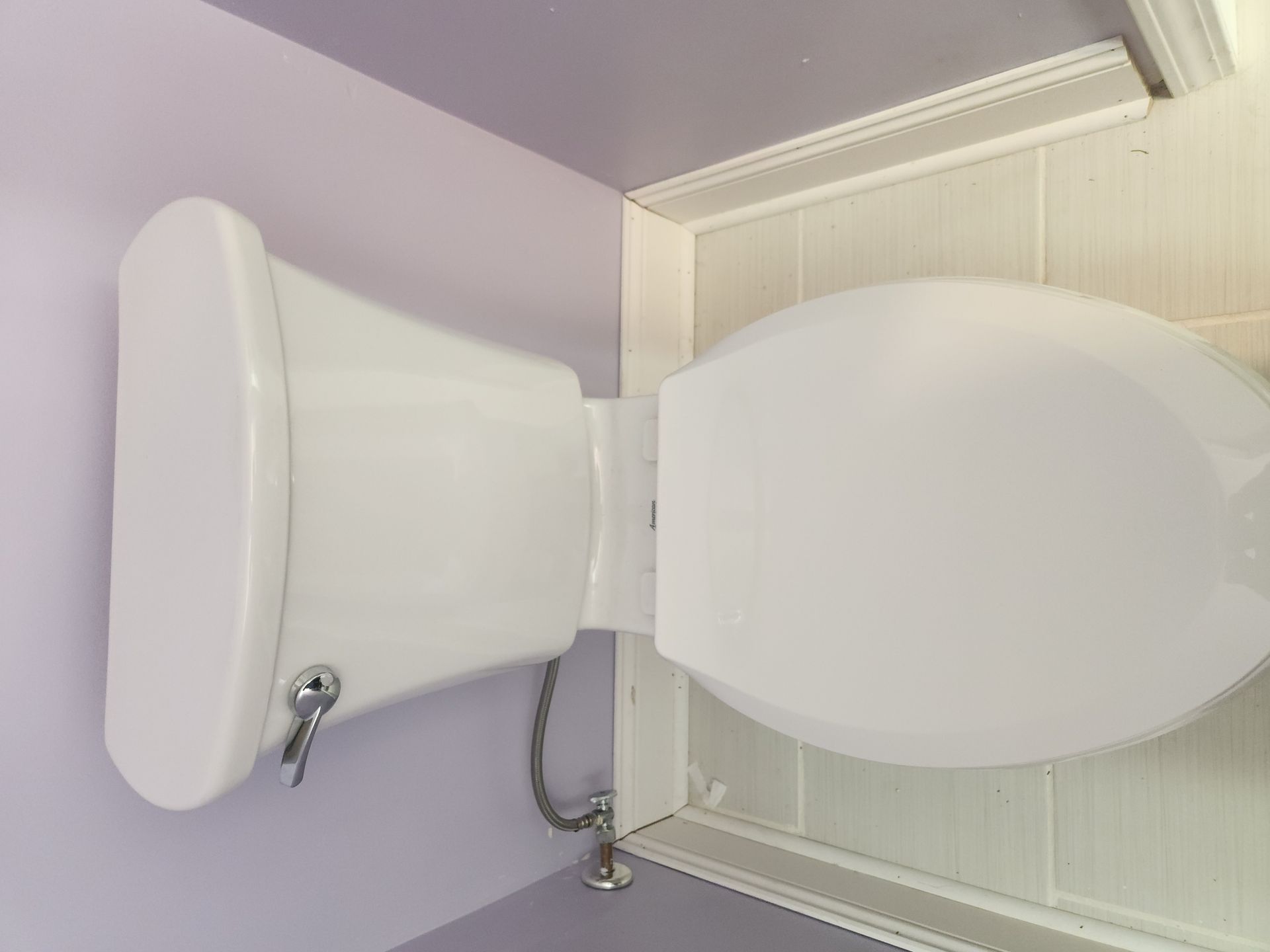 White toilet in a lavender bathroom, viewed from above with the lid up and seat closed.