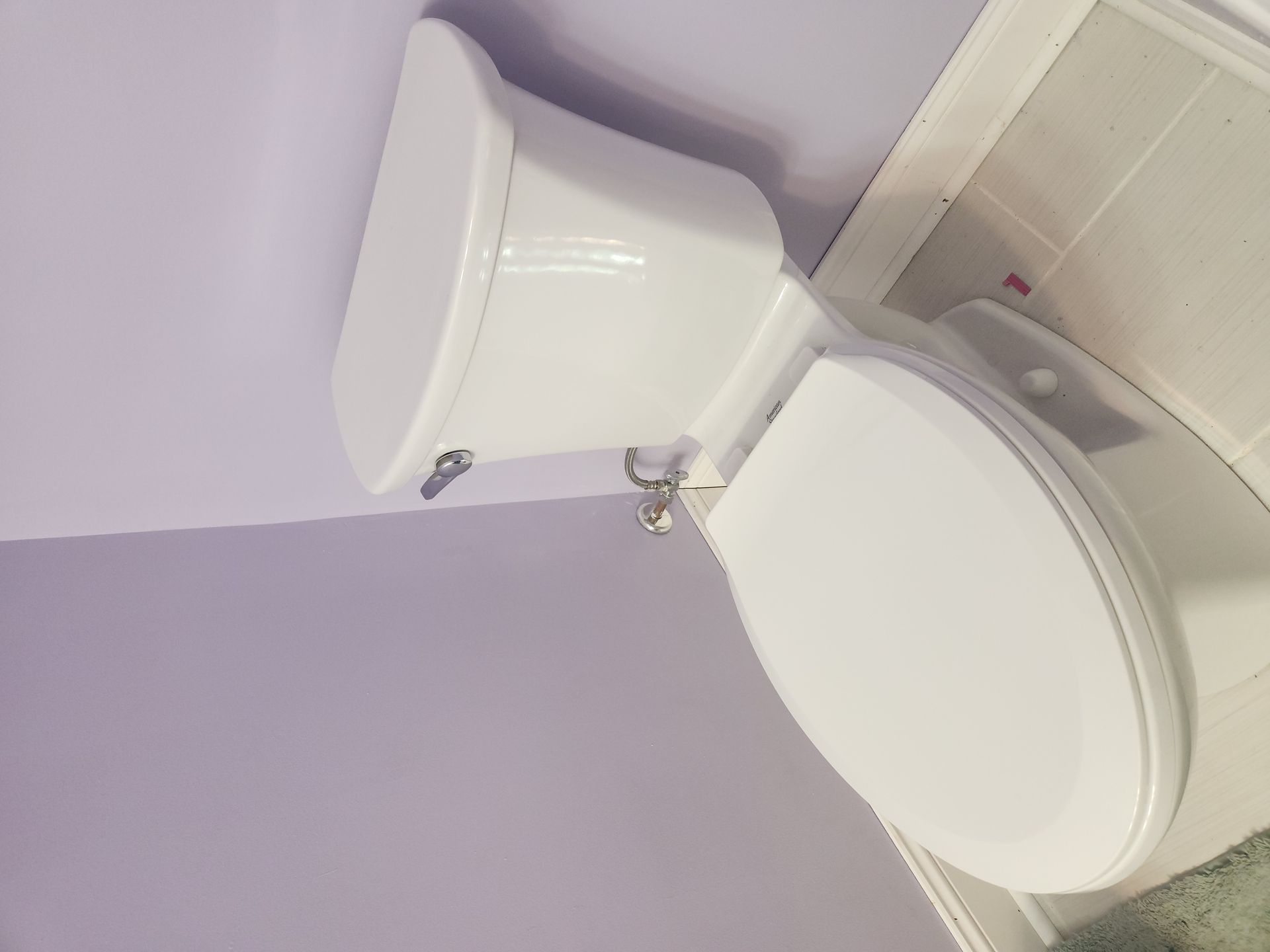 Two white toilets beside a purple wall and tiled floor in a bathroom corner.