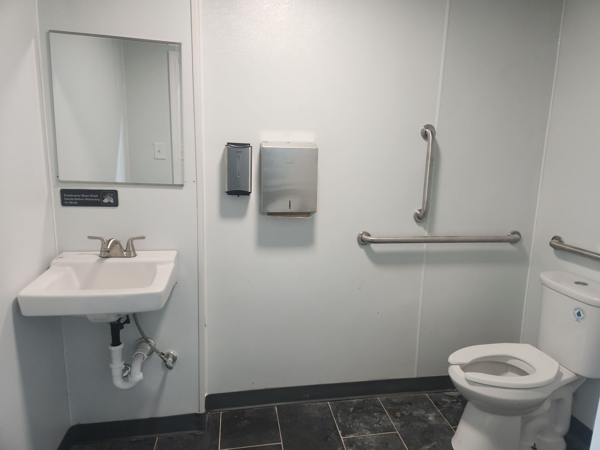 Accessible restroom with sink, mirror, grab bars, soap dispenser, and toilet on the right