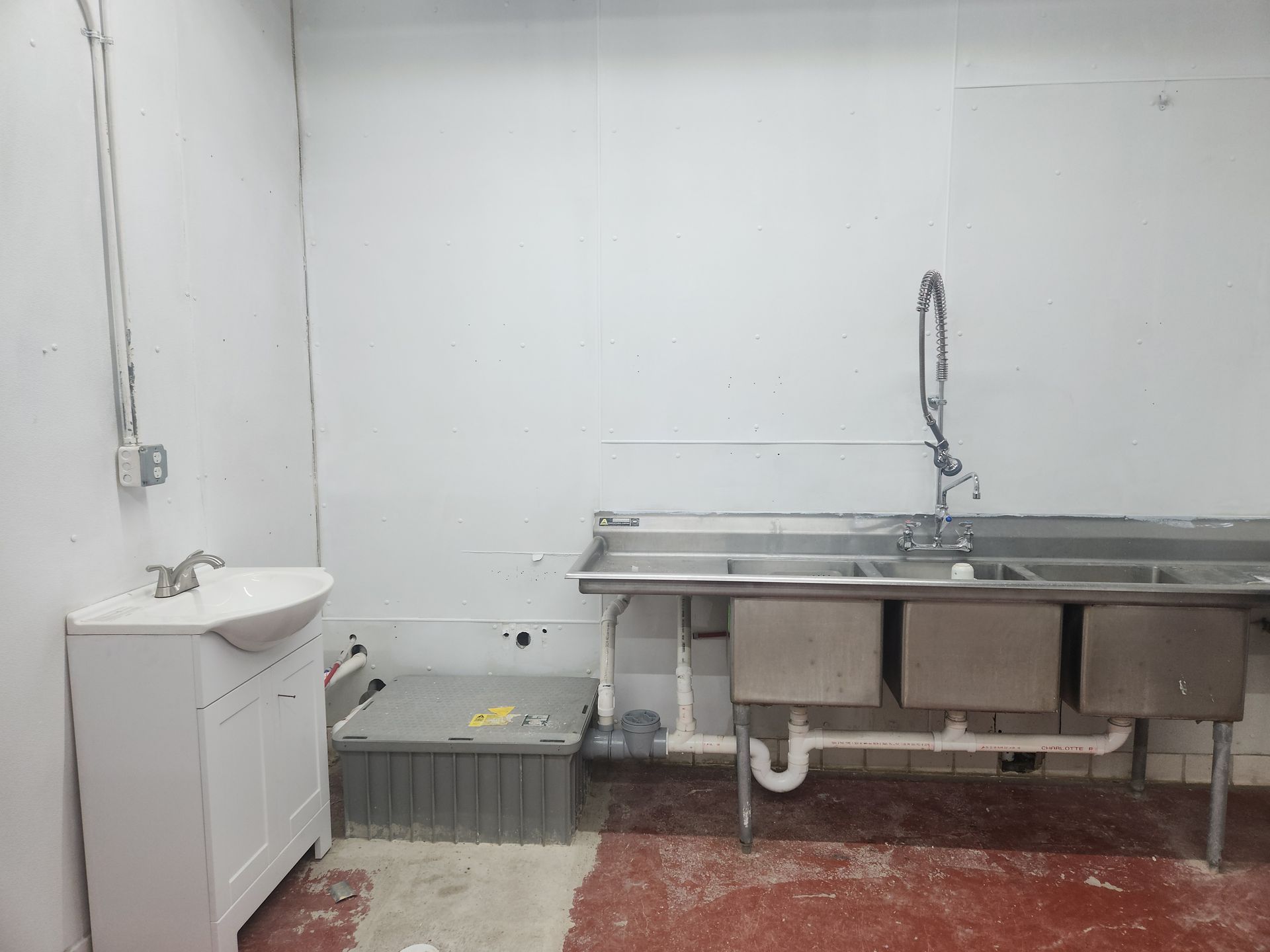 Empty kitchen with stainless steel sink, white cabinets, and tiled floor in a plain room