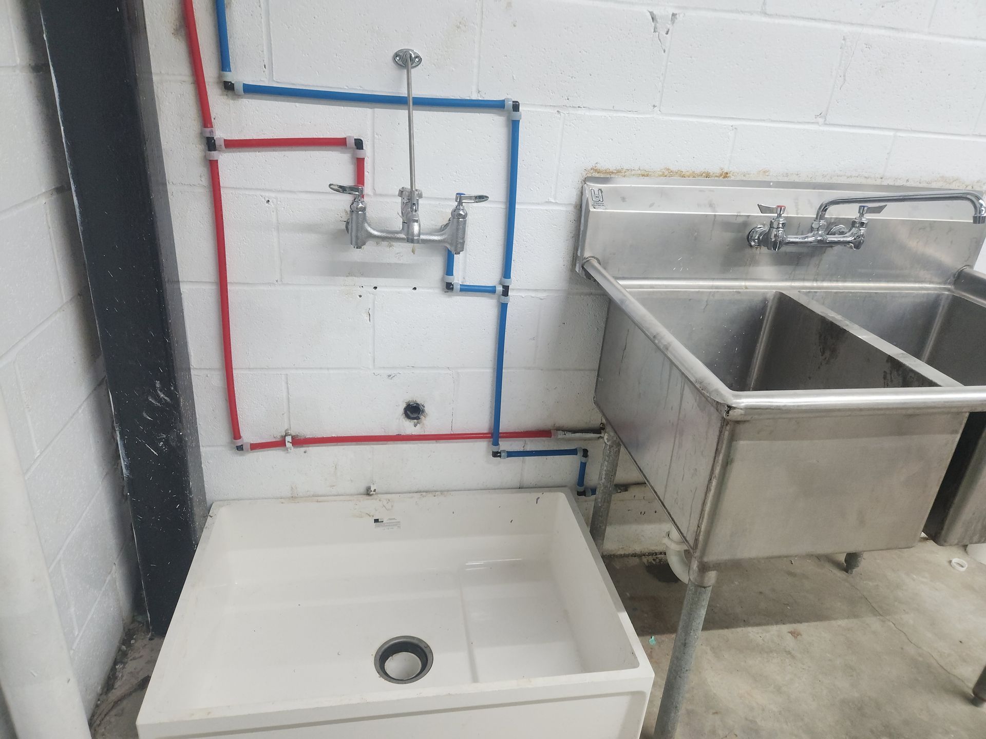 Laundry room utility sink and washing basin with exposed red and blue plumbing lines on a white wall.