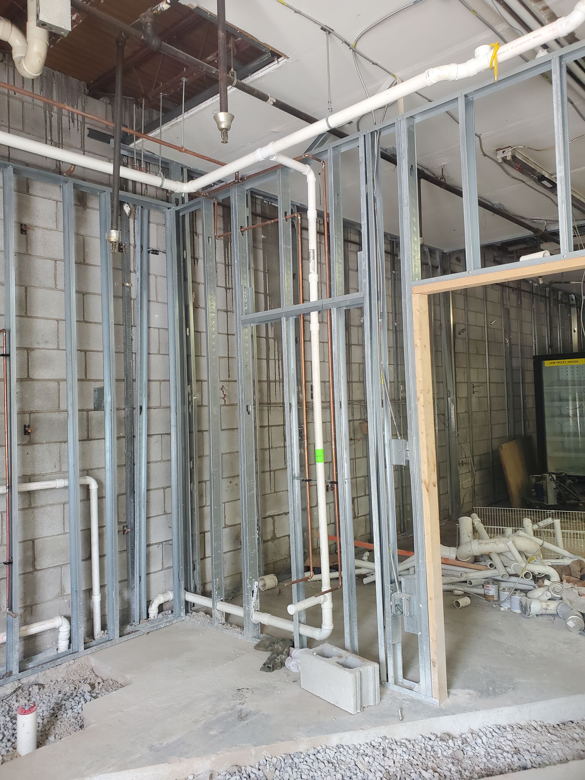 Framed interior construction site with exposed metal studs, wiring, and debris on the floor.