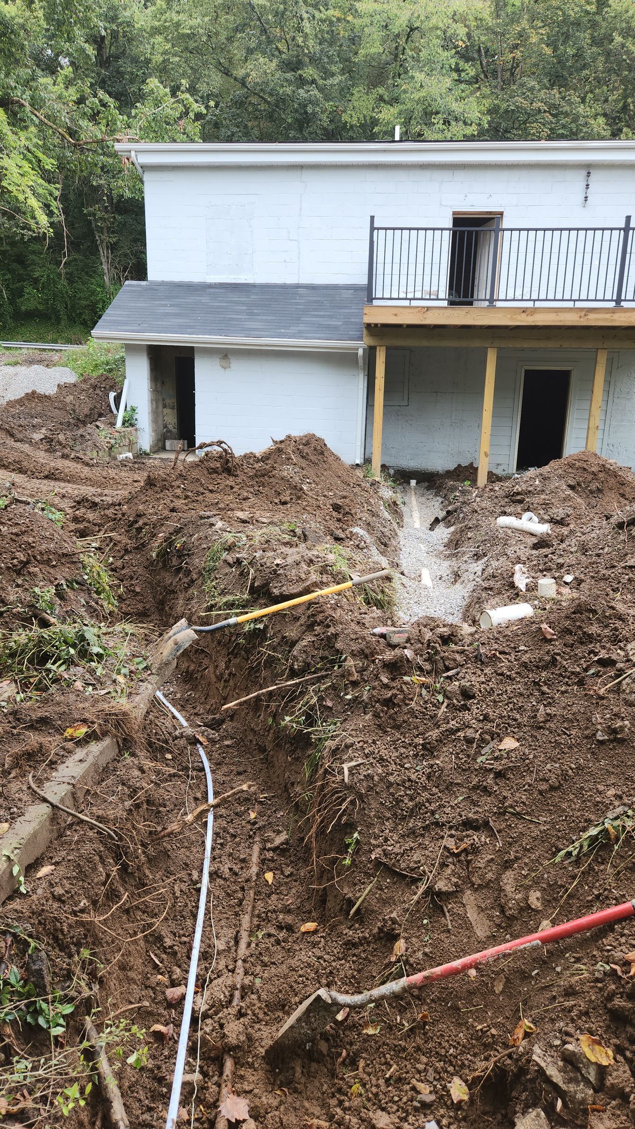 Landslide of mud and debris piled against a white house with a damaged lower level and exposed pipes