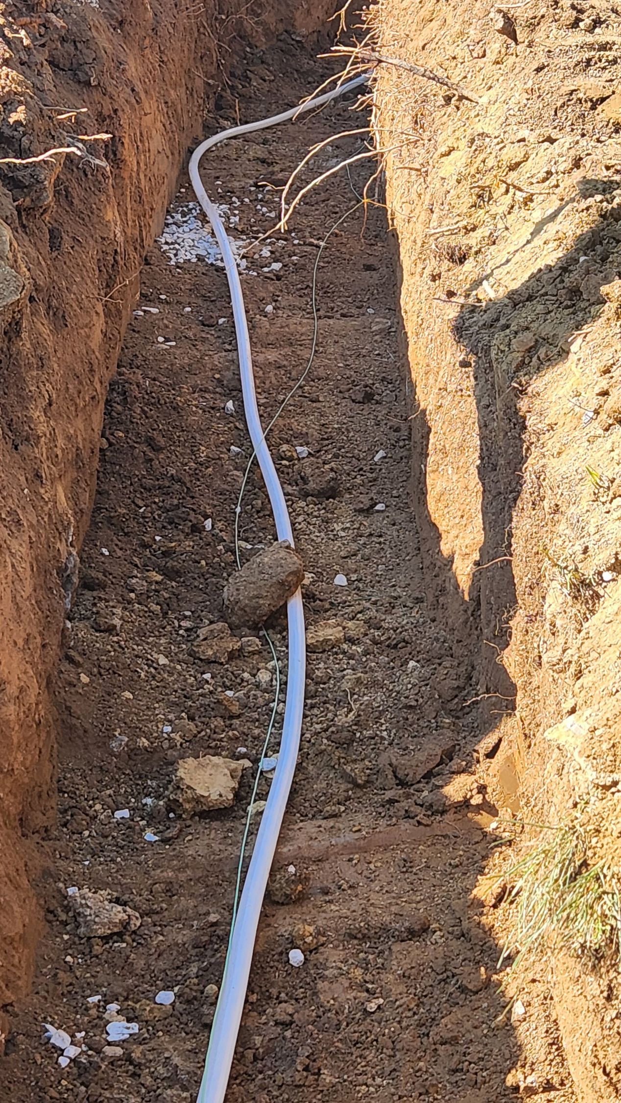 White cable laid in a narrow dirt trench between soil walls.