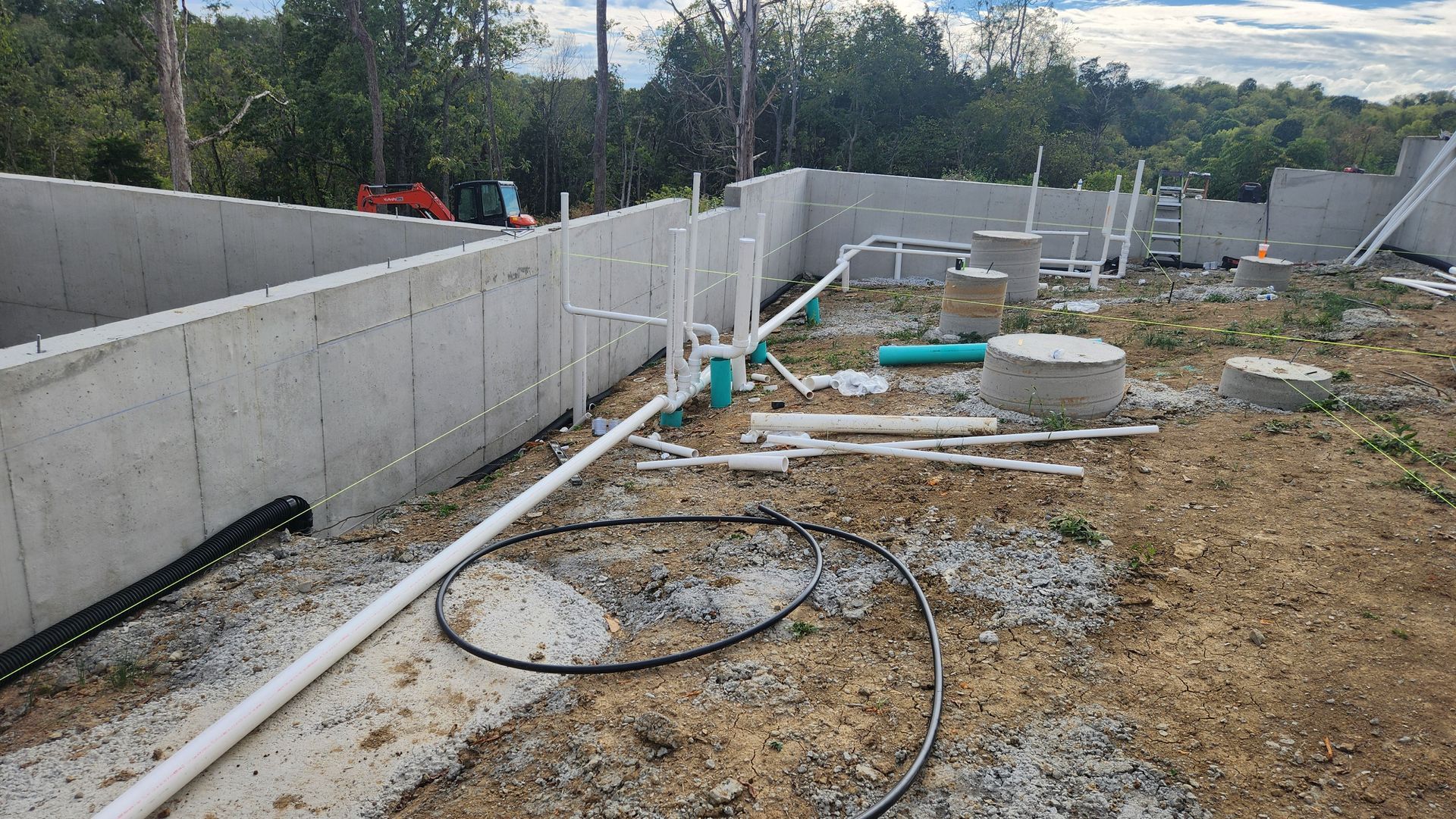Partially built foundation with concrete walls, scattered pipes, and construction debris on a muddy lot