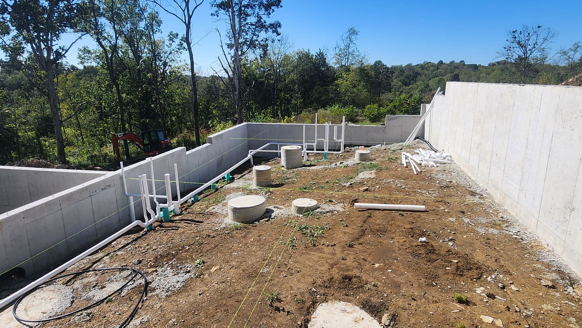 Empty backyard construction area with dirt ground, concrete walls, and scattered pipes under a clear sky