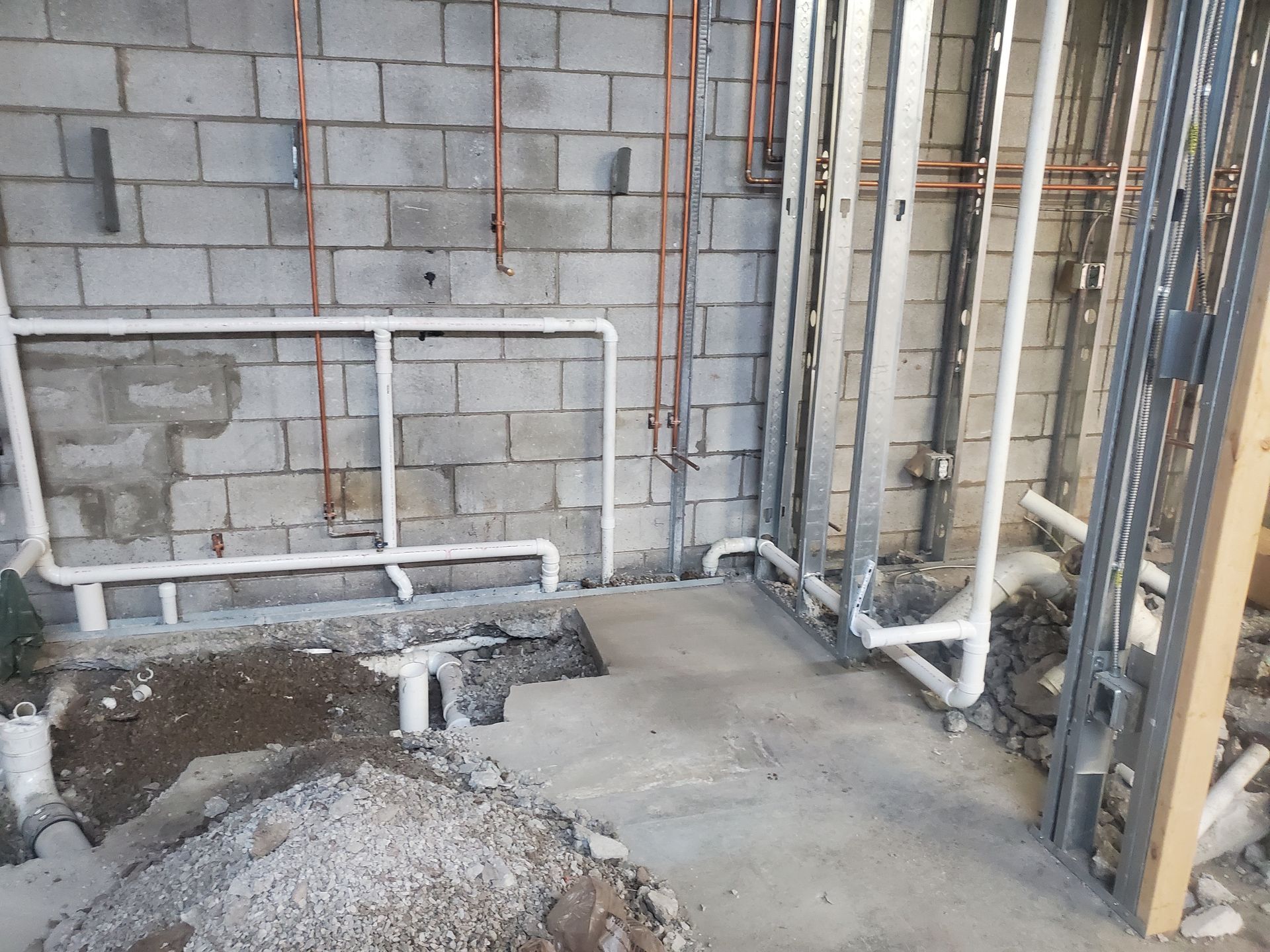 Partially finished utility room with cinder block wall, exposed pipes, and unfinished concrete floor