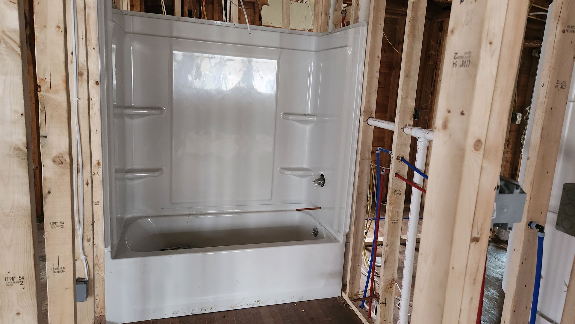 Bathtub with shower surround installed in an unfinished room with exposed wall studs and plumbing.