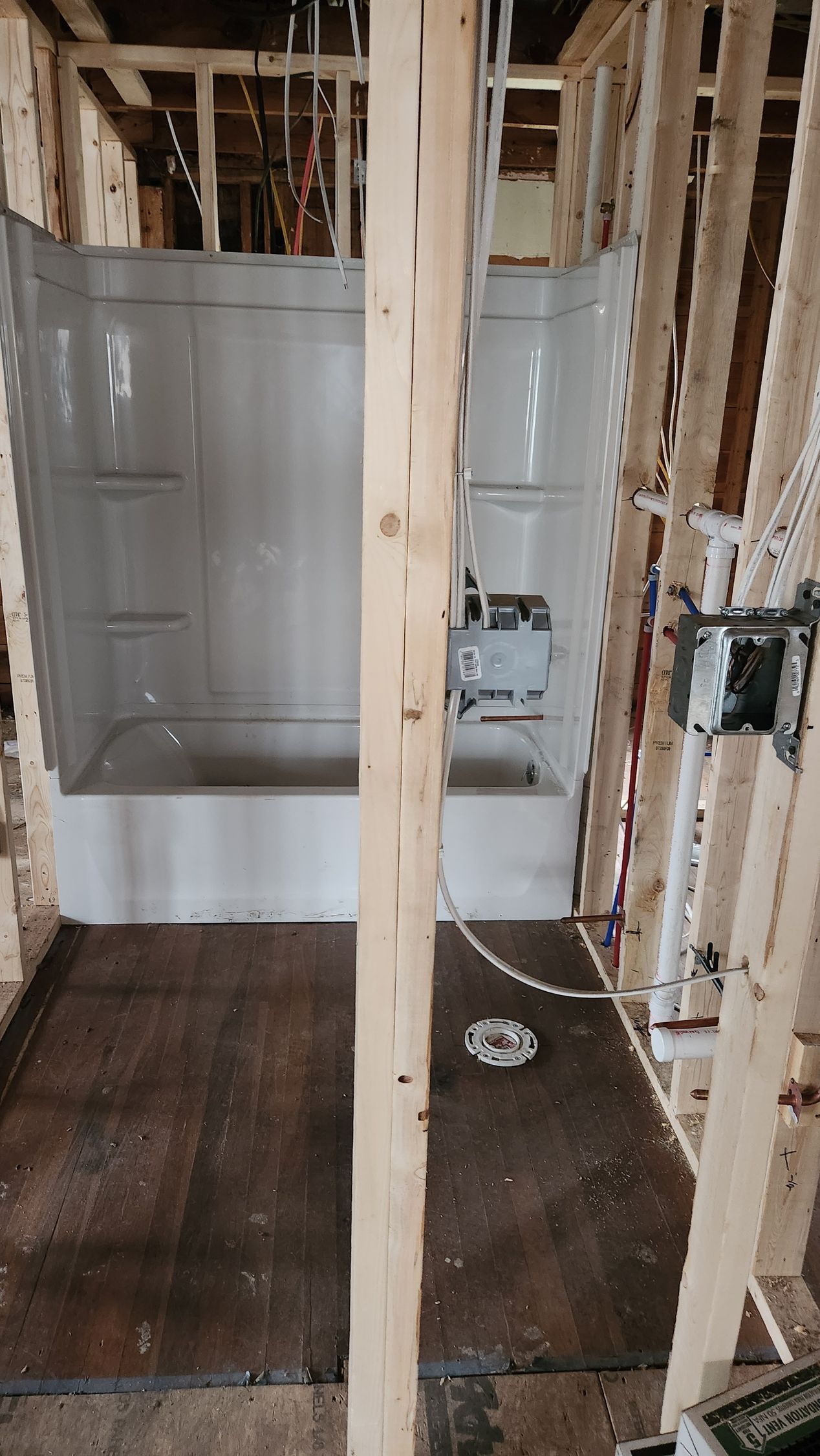 Bathroom under renovation with exposed studs, a bathtub, and unfinished flooring.