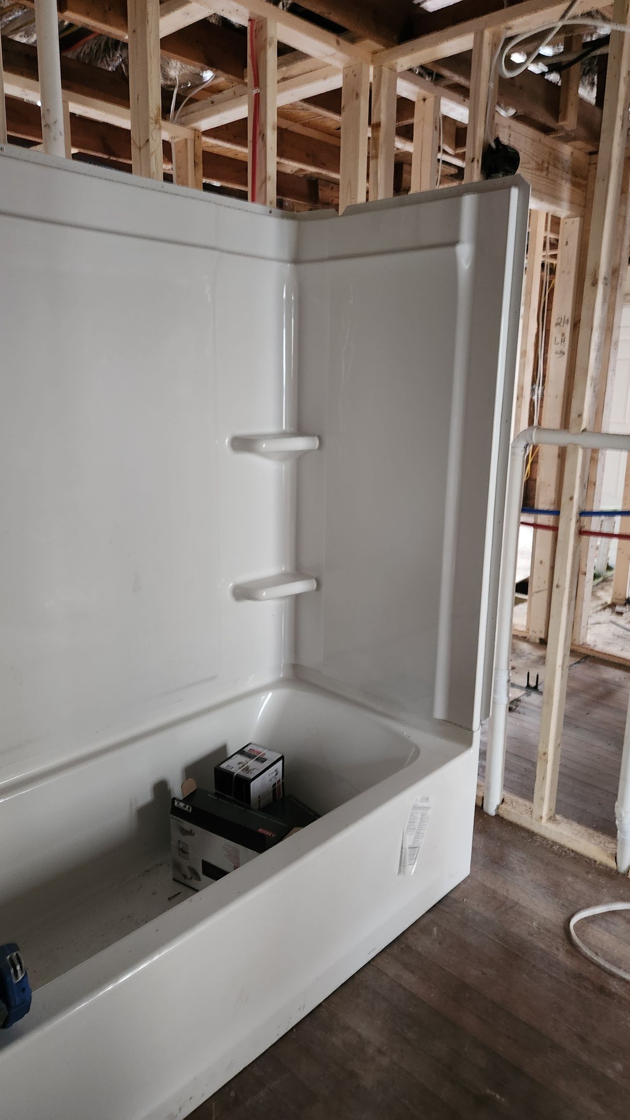 Partially tiled shower under construction with white walls, built-in bench, and exposed framing above