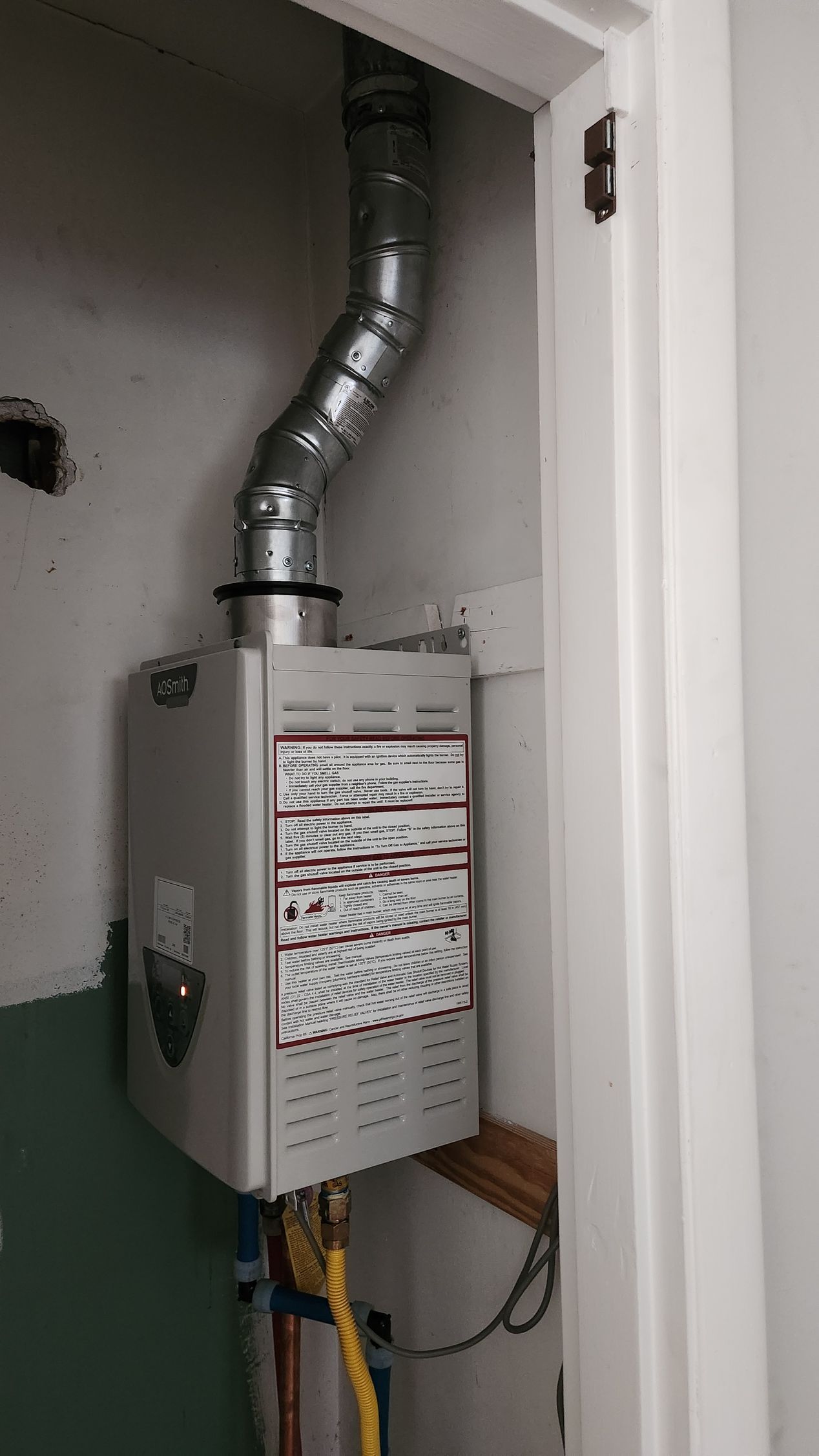 Wall-mounted utility meter box with a silver ventilation pipe in a small closet-like space