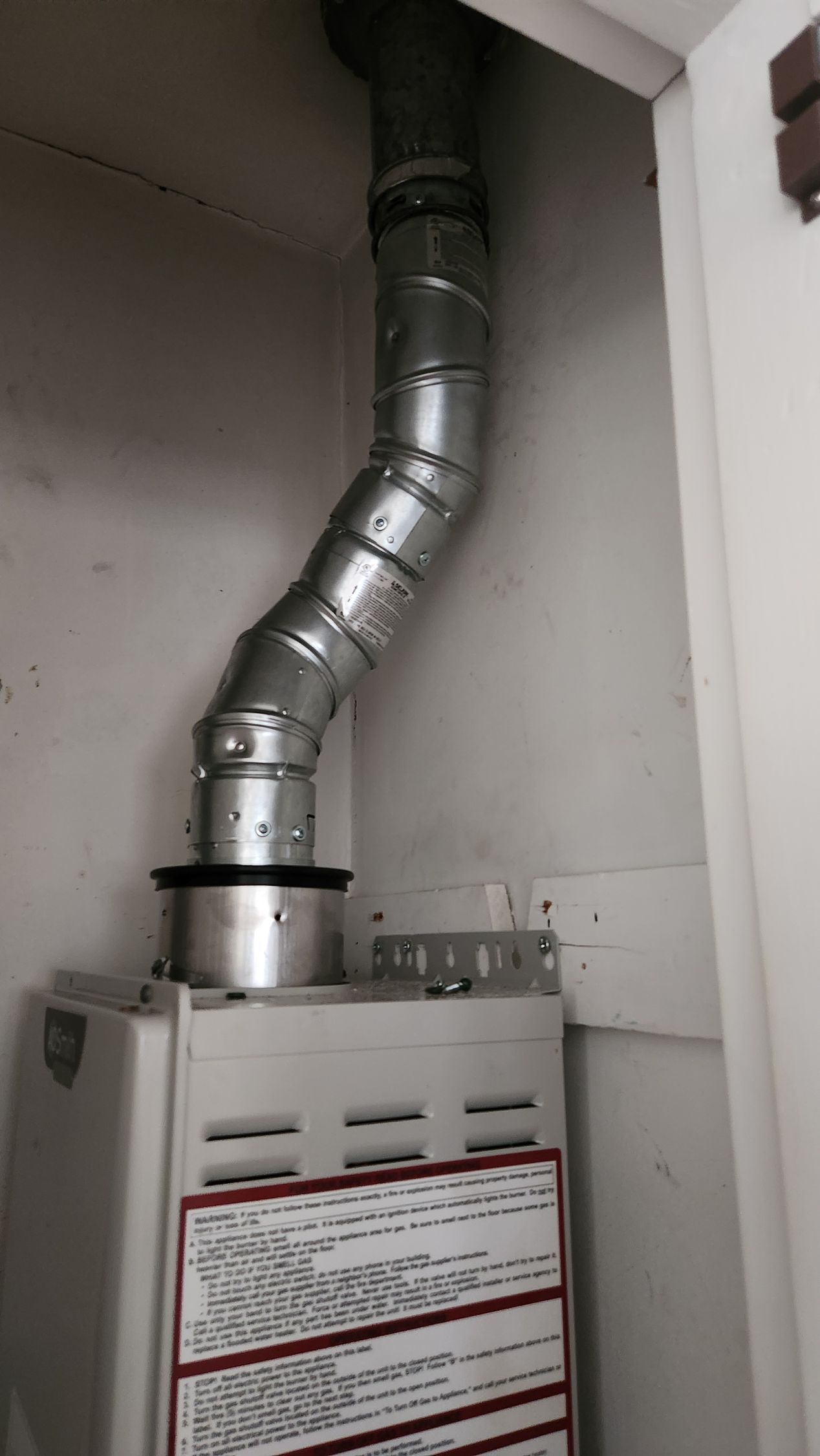 Silver vent pipe connected to a white furnace in a narrow utility closet