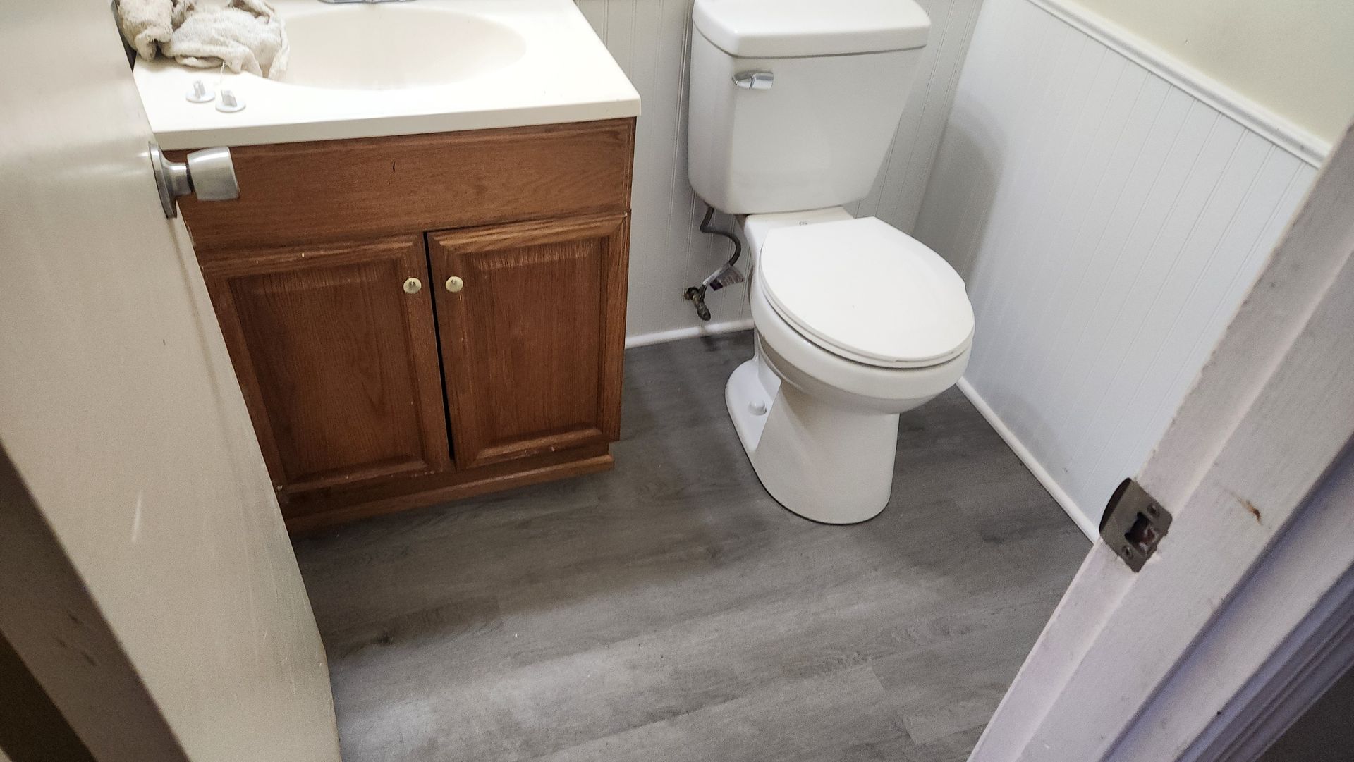 Small bathroom with toilet, wood vanity, white sink, and gray flooring.