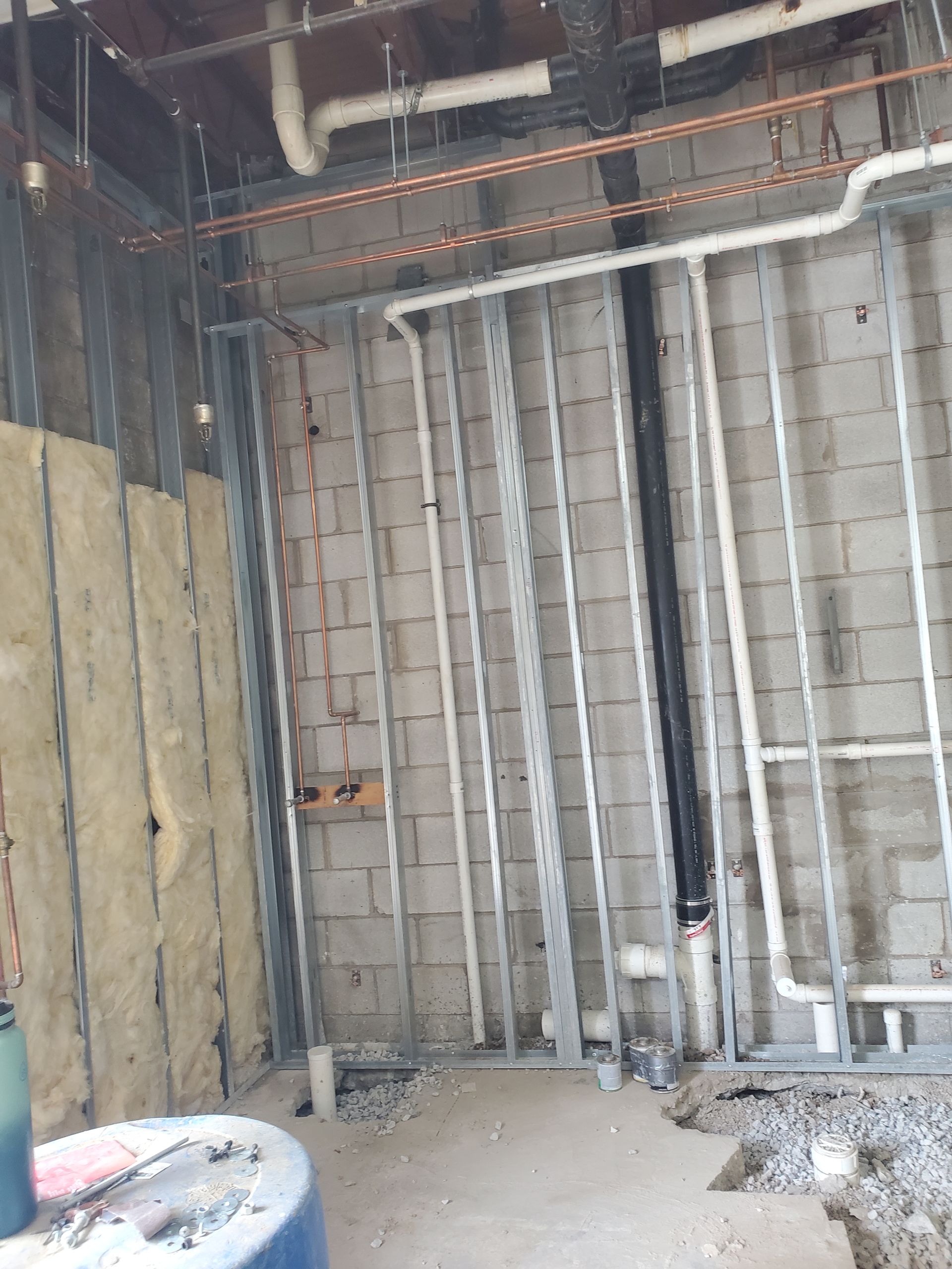 Unfinished interior wall framing with exposed insulation, pipes, and construction debris.