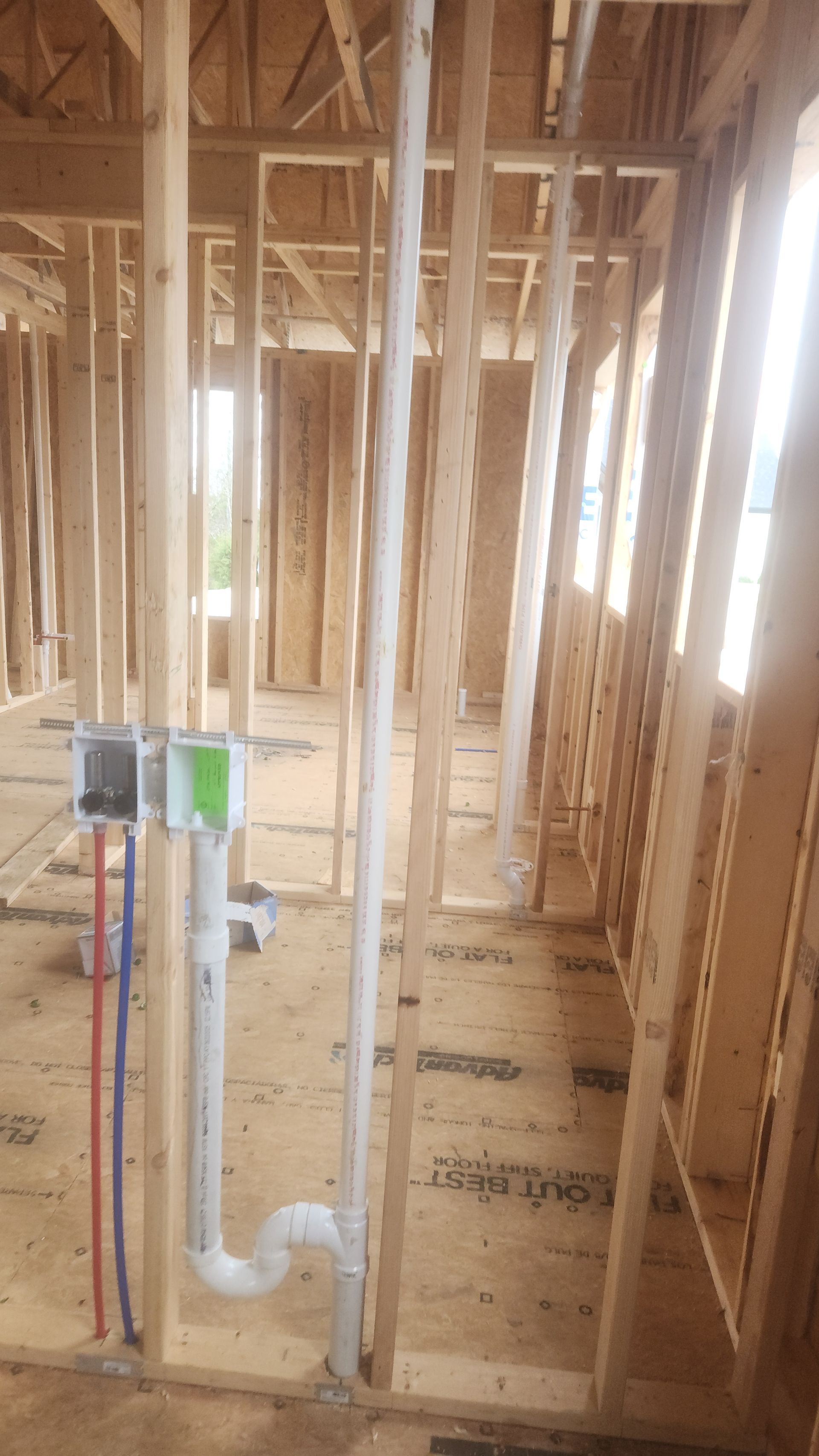 Interior of a house under construction with exposed wooden framing and plumbing pipes in the foreground