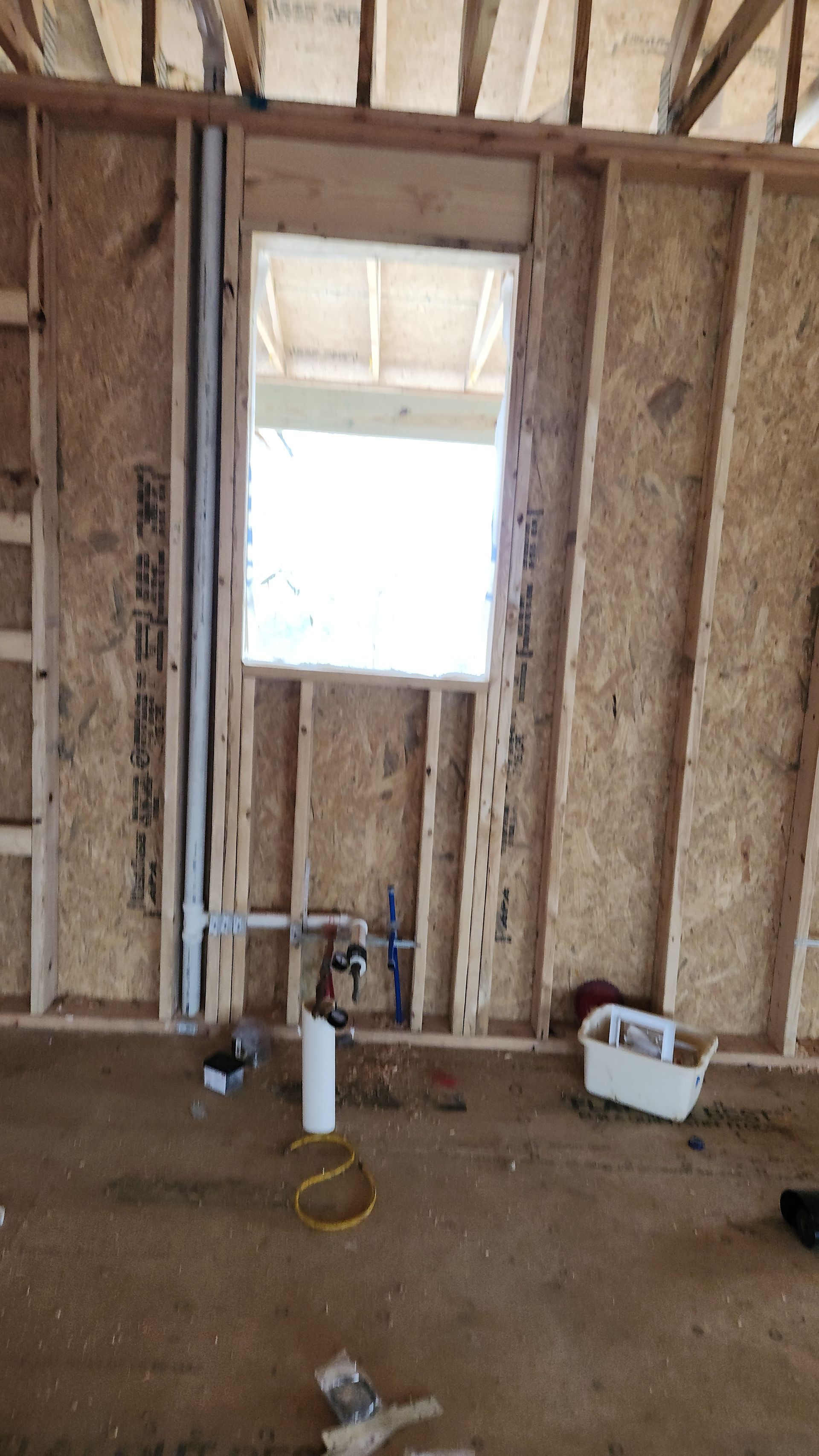 Unfinished room with exposed wall studs, a small window, and construction materials on the floor.
