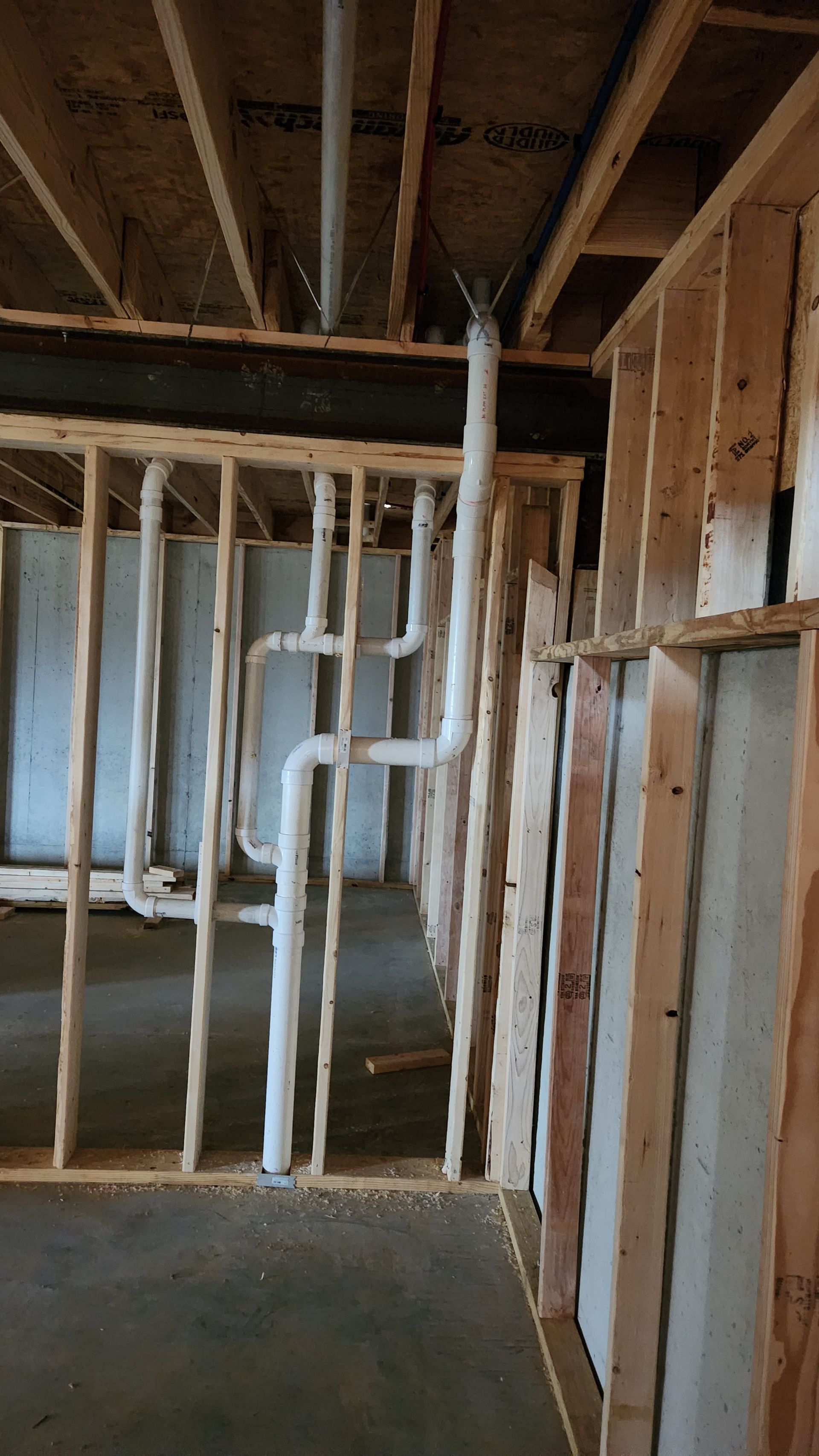 Exposed basement framing with plumbing pipes and unfinished walls under construction
