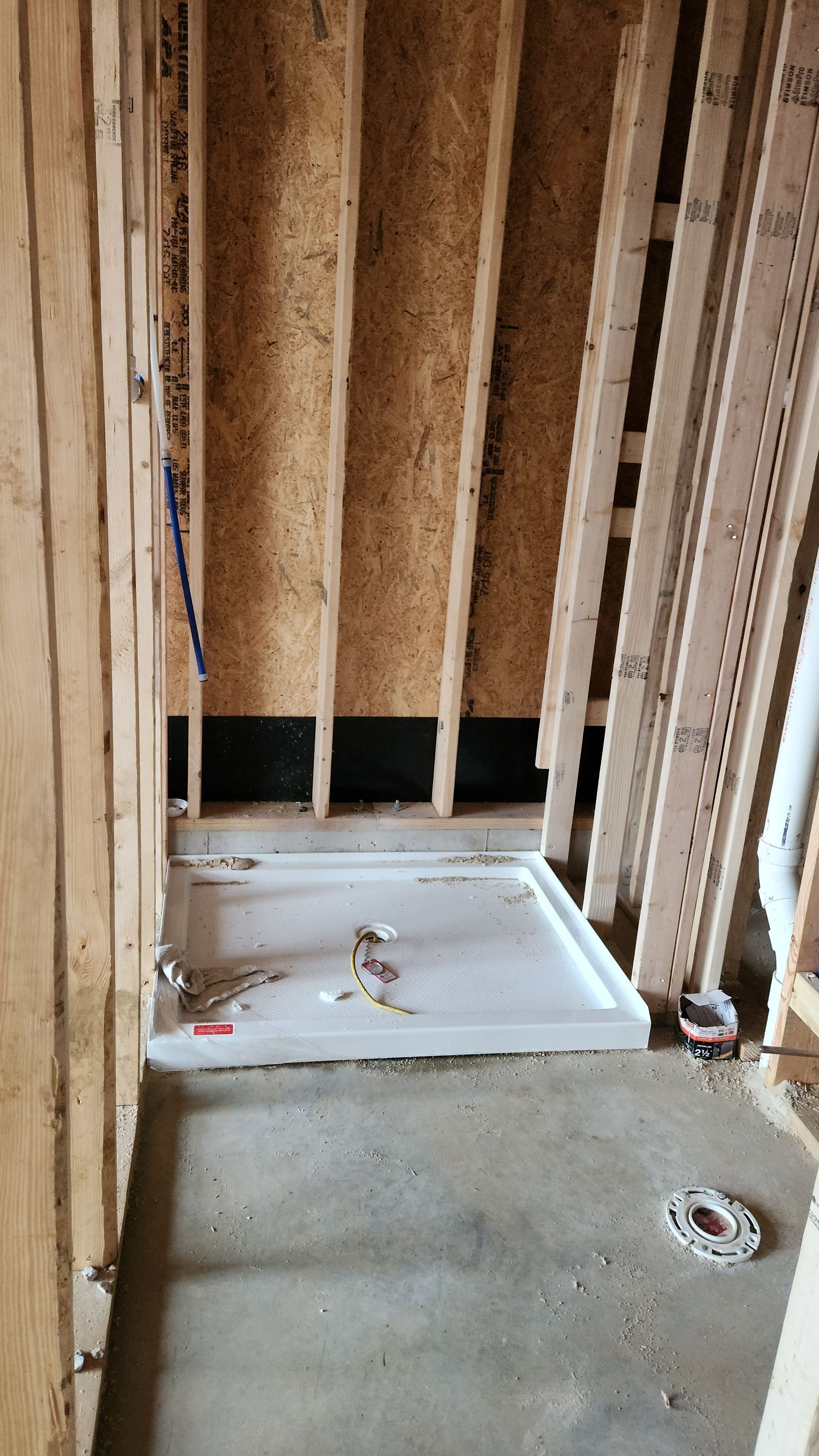 Unfinished bathroom with exposed studs, a white shower base, and concrete floor.