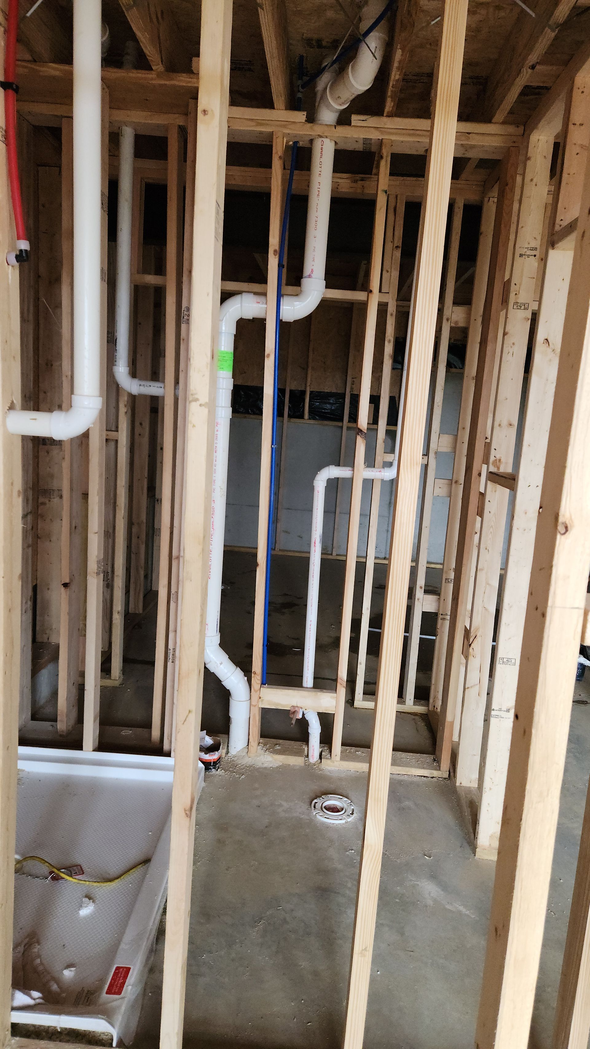Unfinished interior wall framing with white PVC pipes and a concrete floor during construction.
