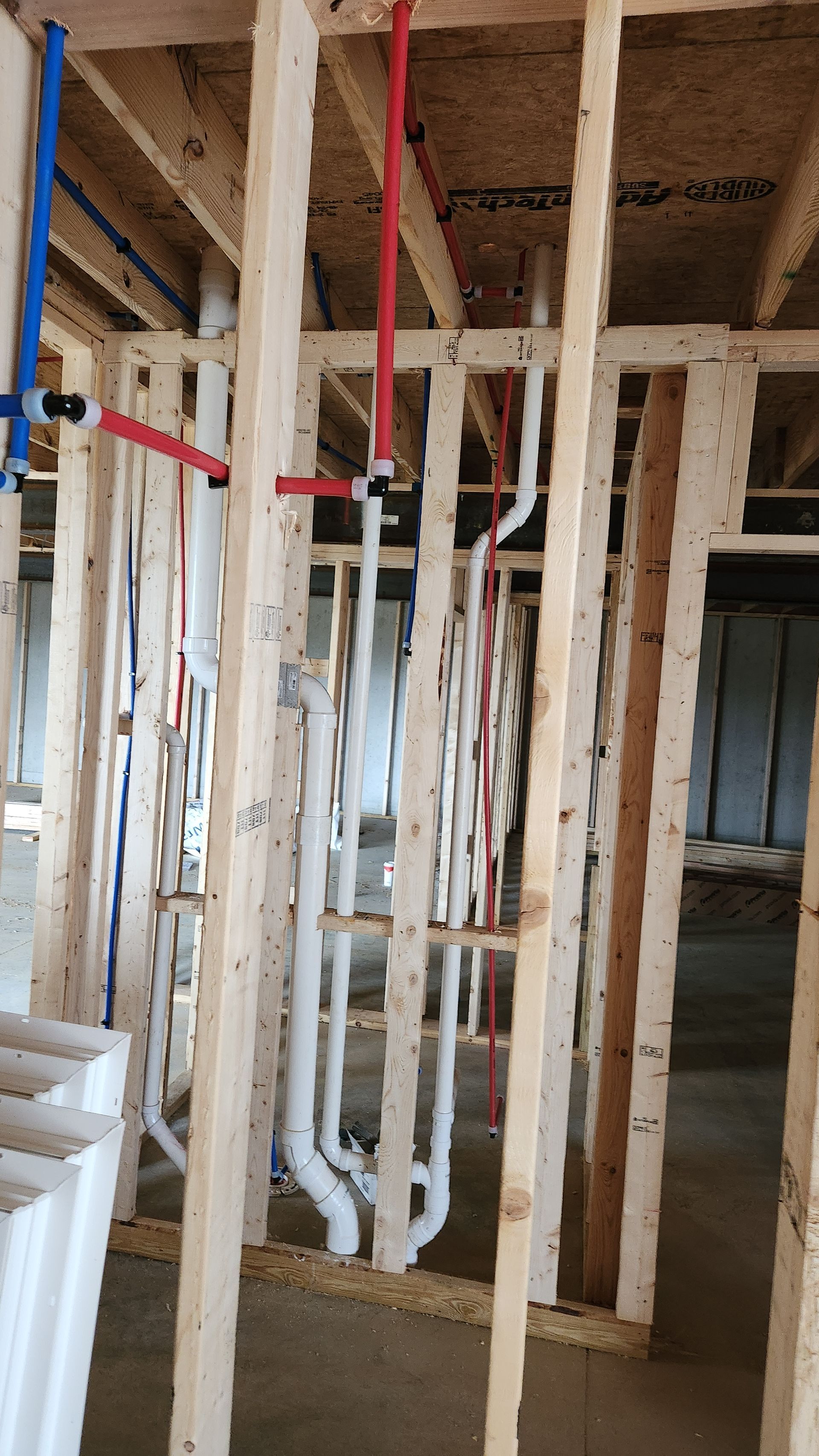 Framed interior wall with exposed wooden studs and white plumbing pipes under construction