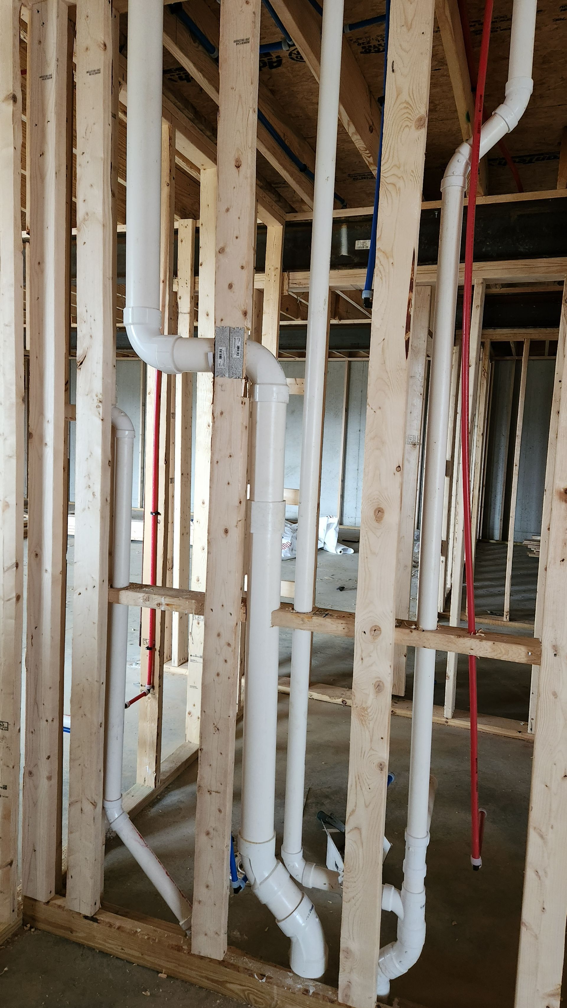 Unfinished house framing with exposed white PVC plumbing pipes and red electrical wires in the walls.