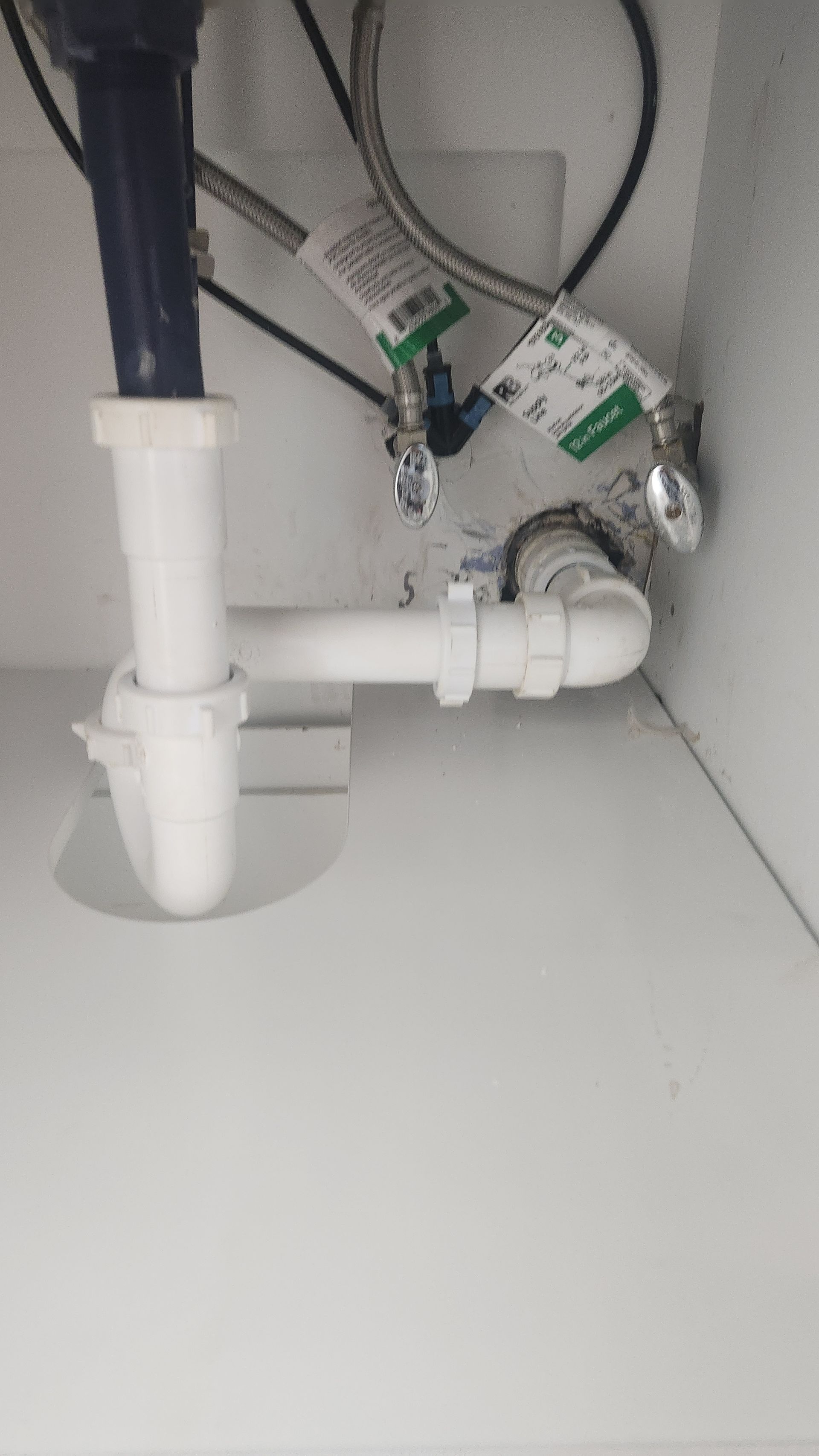 Under-sink plumbing with white pipes, a drain trap, and valves inside a cabinet