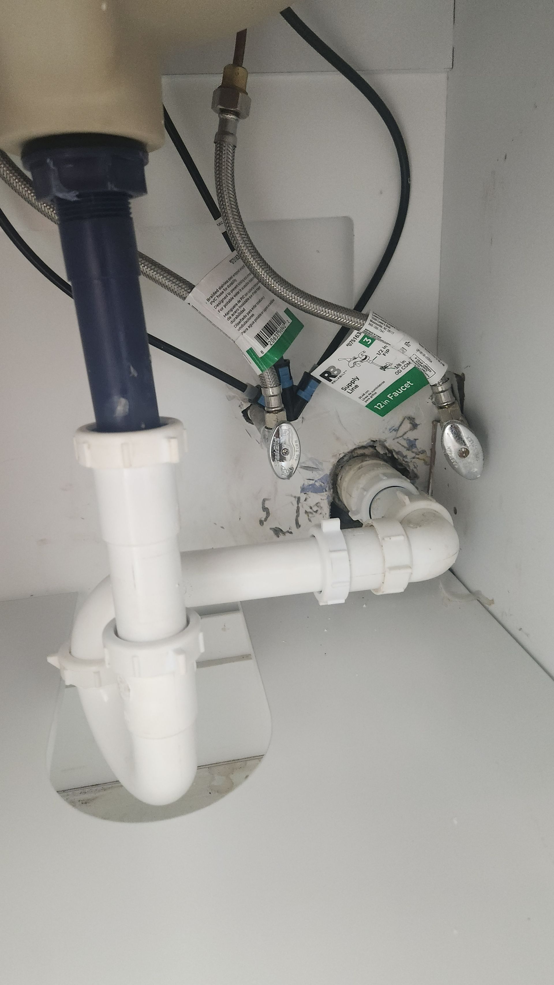 Under-sink plumbing with white PVC drain pipes, a blue pipe, and a flexible hose inside a cabinet