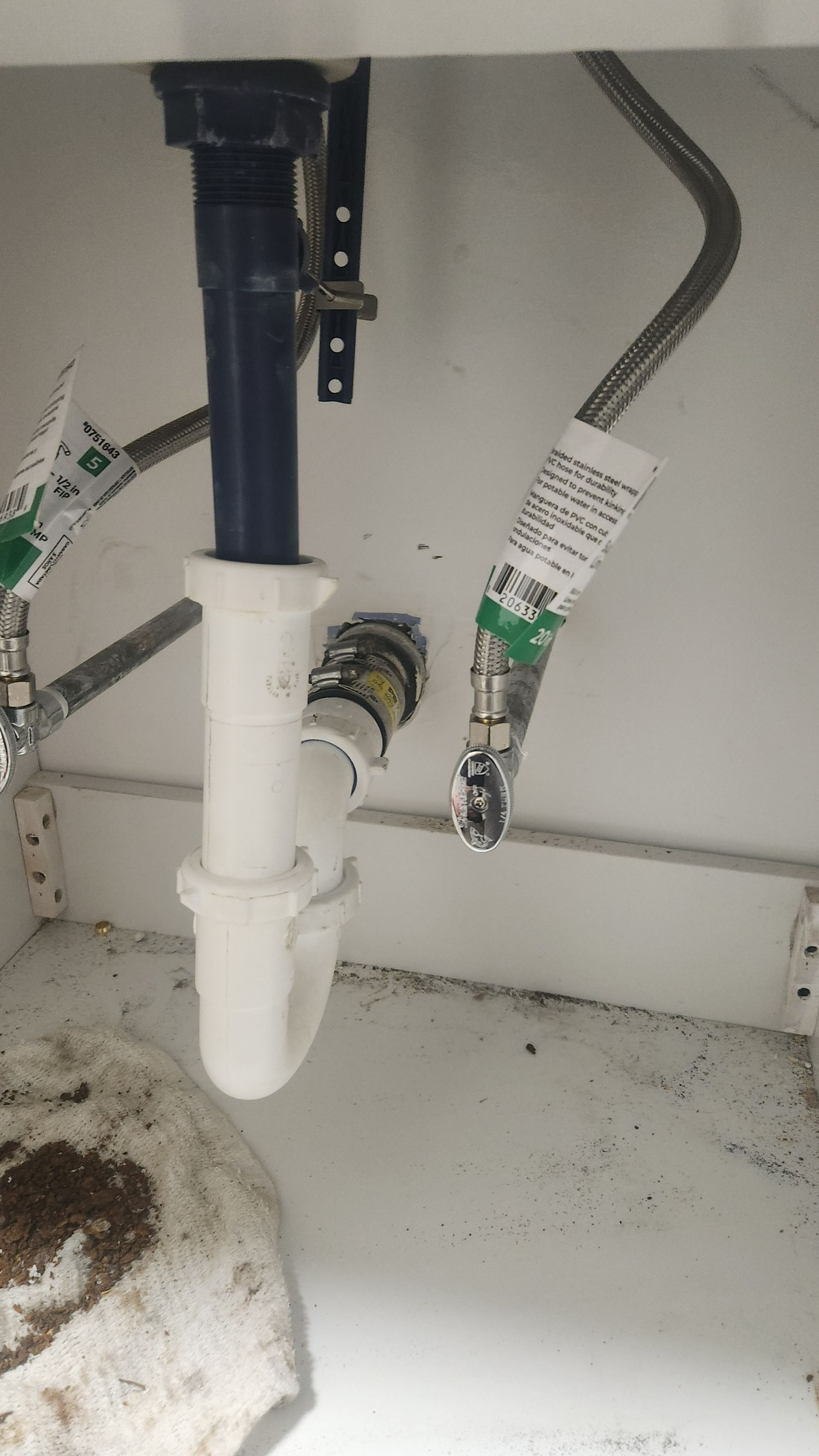 Under-sink plumbing with white PVC drain pipes and braided water supply lines inside a cabinet