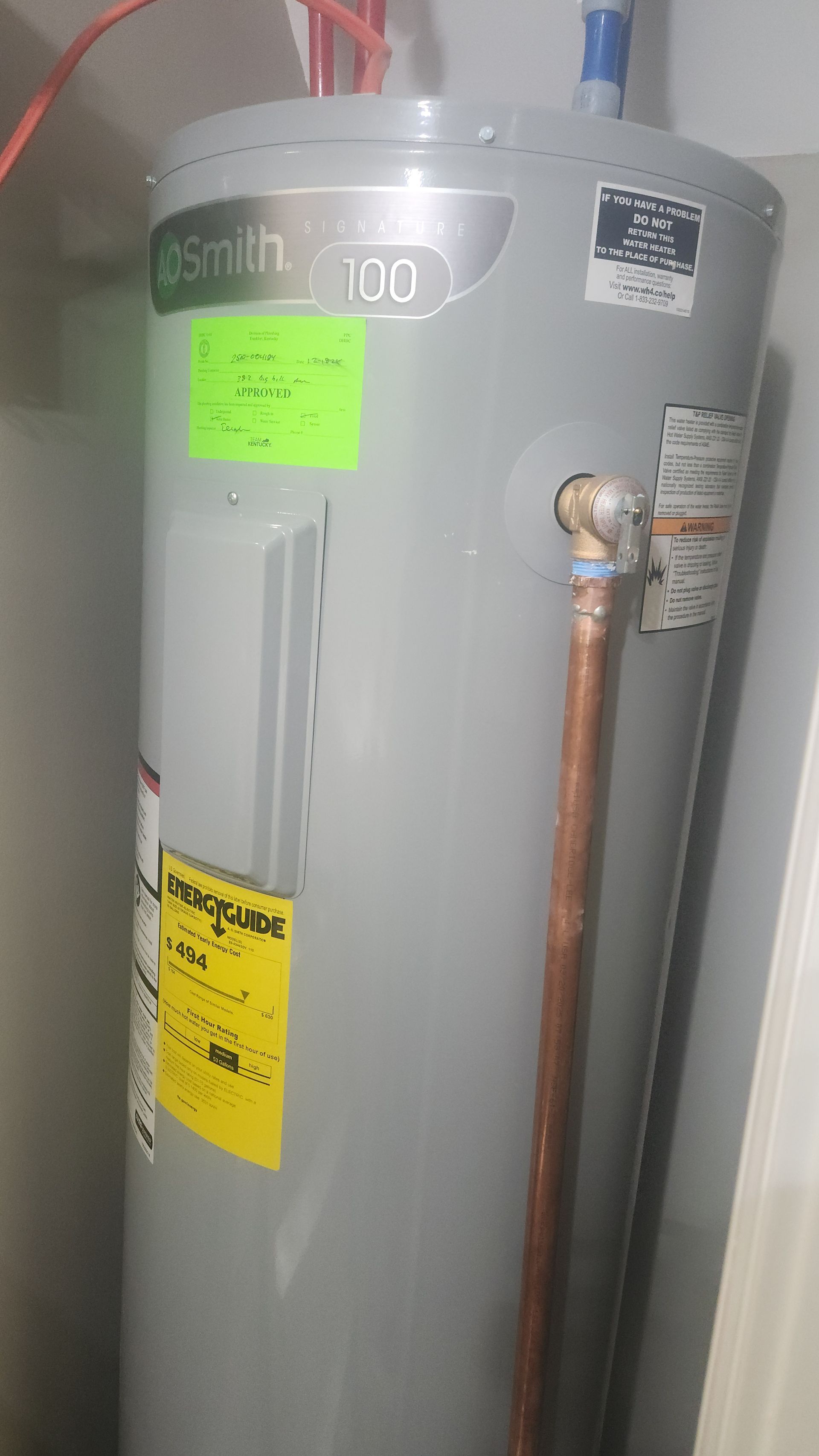 Gray water heater with yellow labels and copper pipe in a utility closet