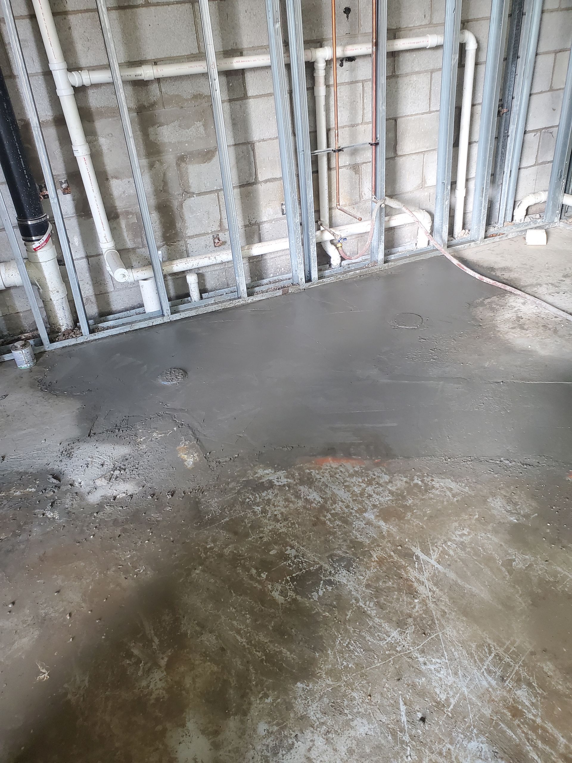 Unfinished room with exposed wall framing and a wet concrete floor covered in puddles.