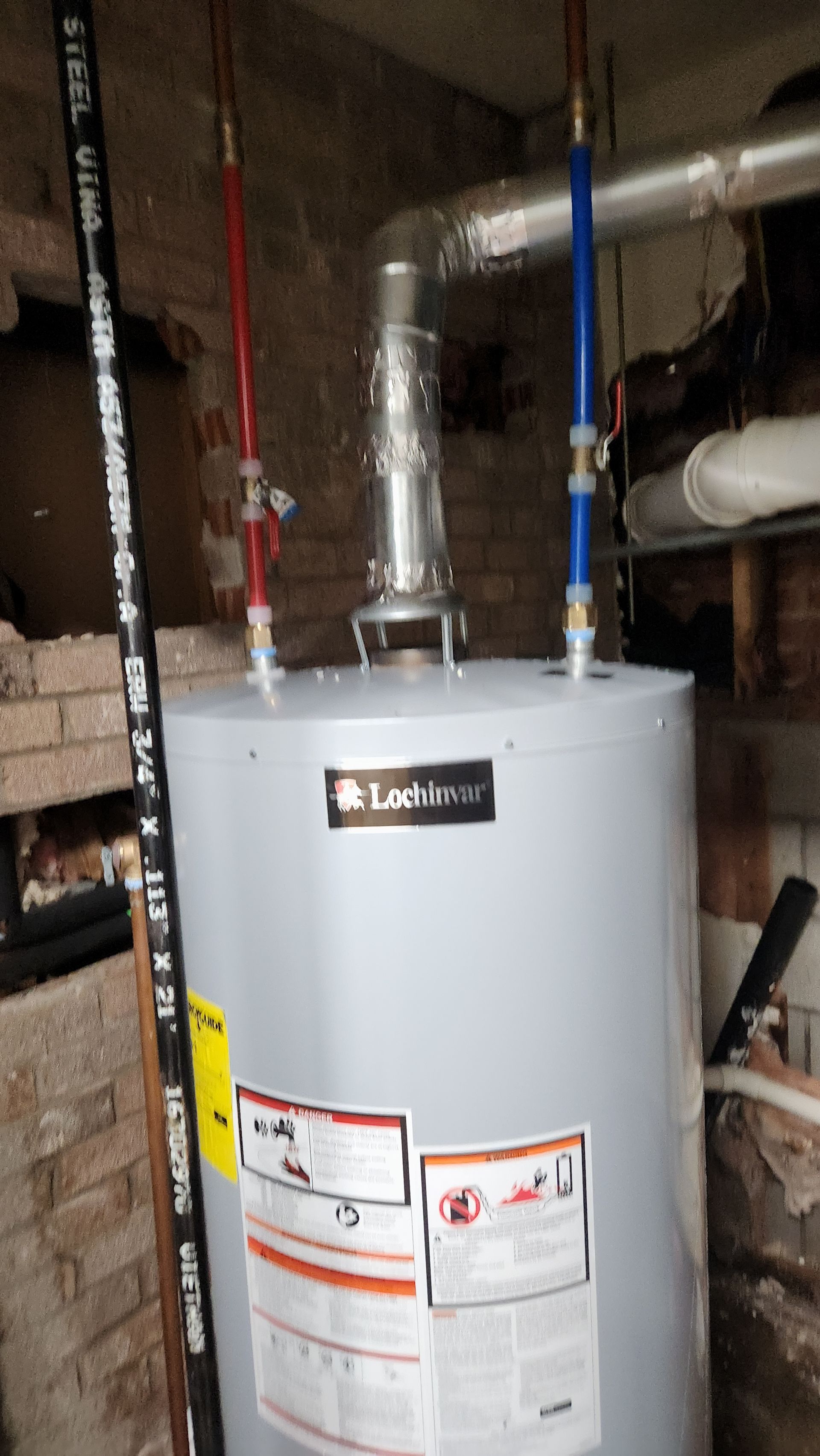 White water heater with red and blue pipes in a basement utility area