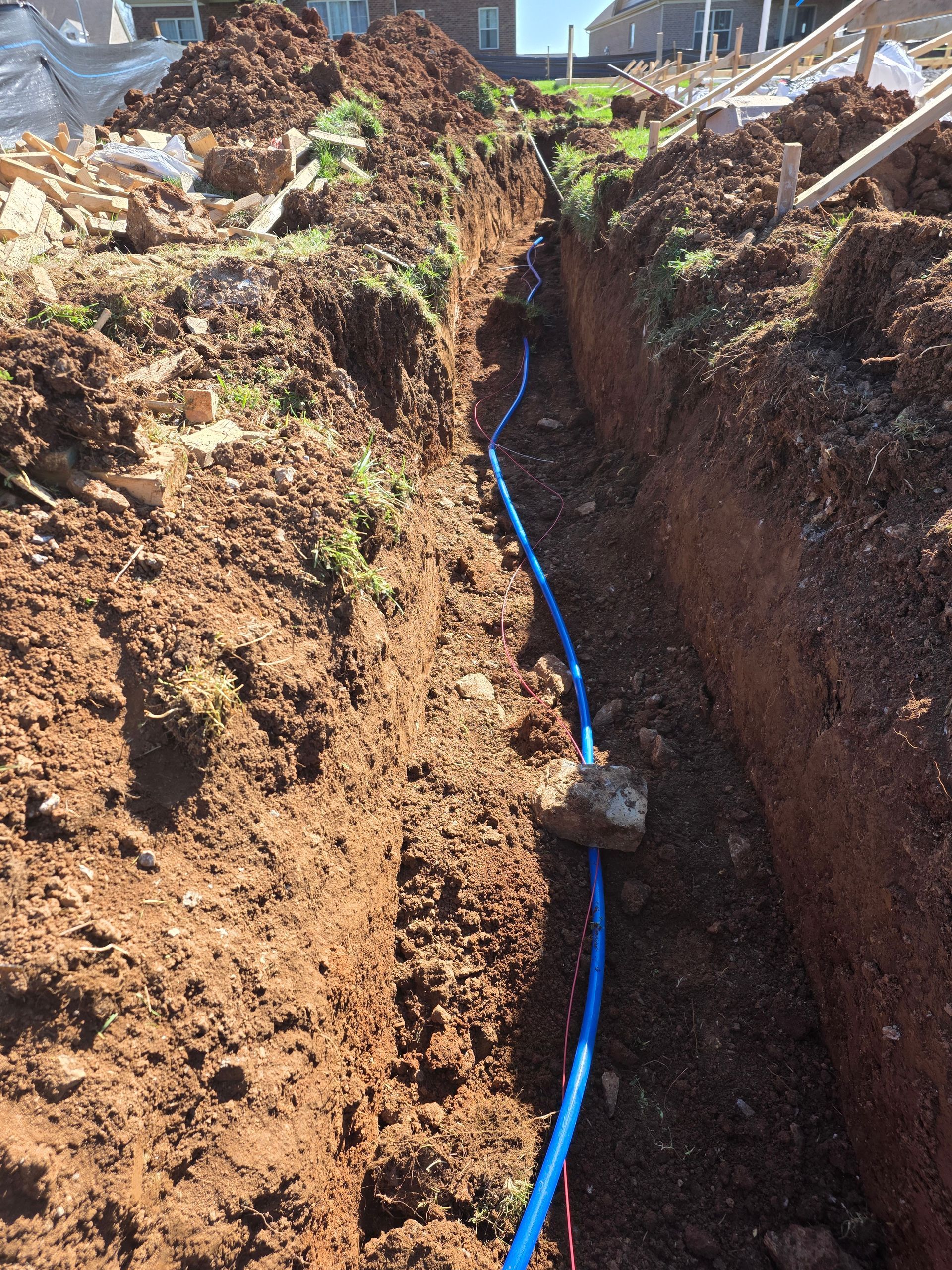 Trenched dirt path with a blue utility cable running through the center of a construction site.