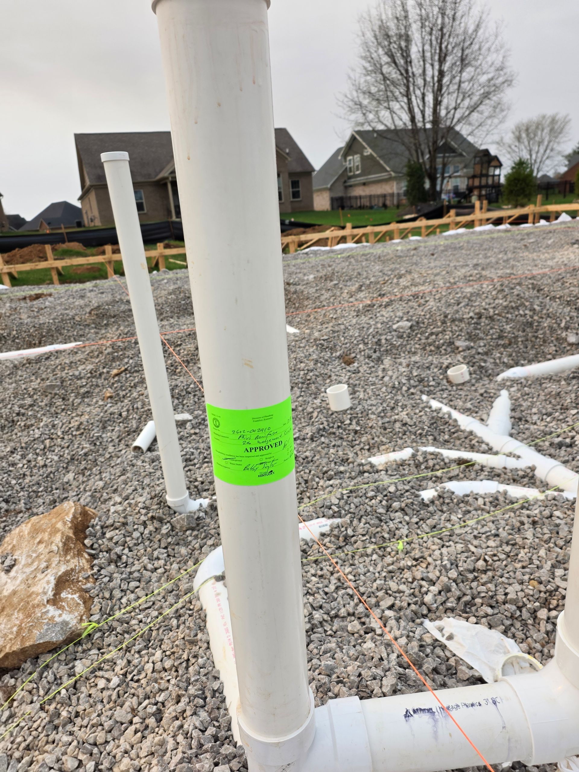 White PVC pipe with neon green label in gravel construction site near houses