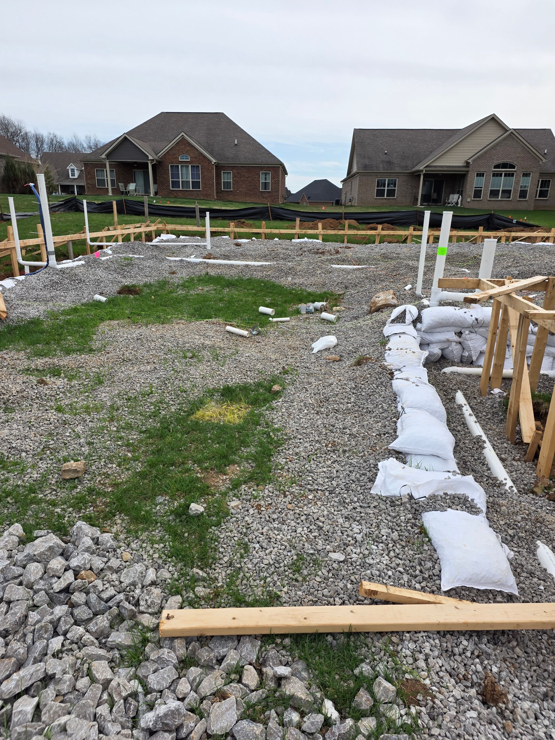 Gravel construction site with white edging, wooden stakes, and houses in the background.