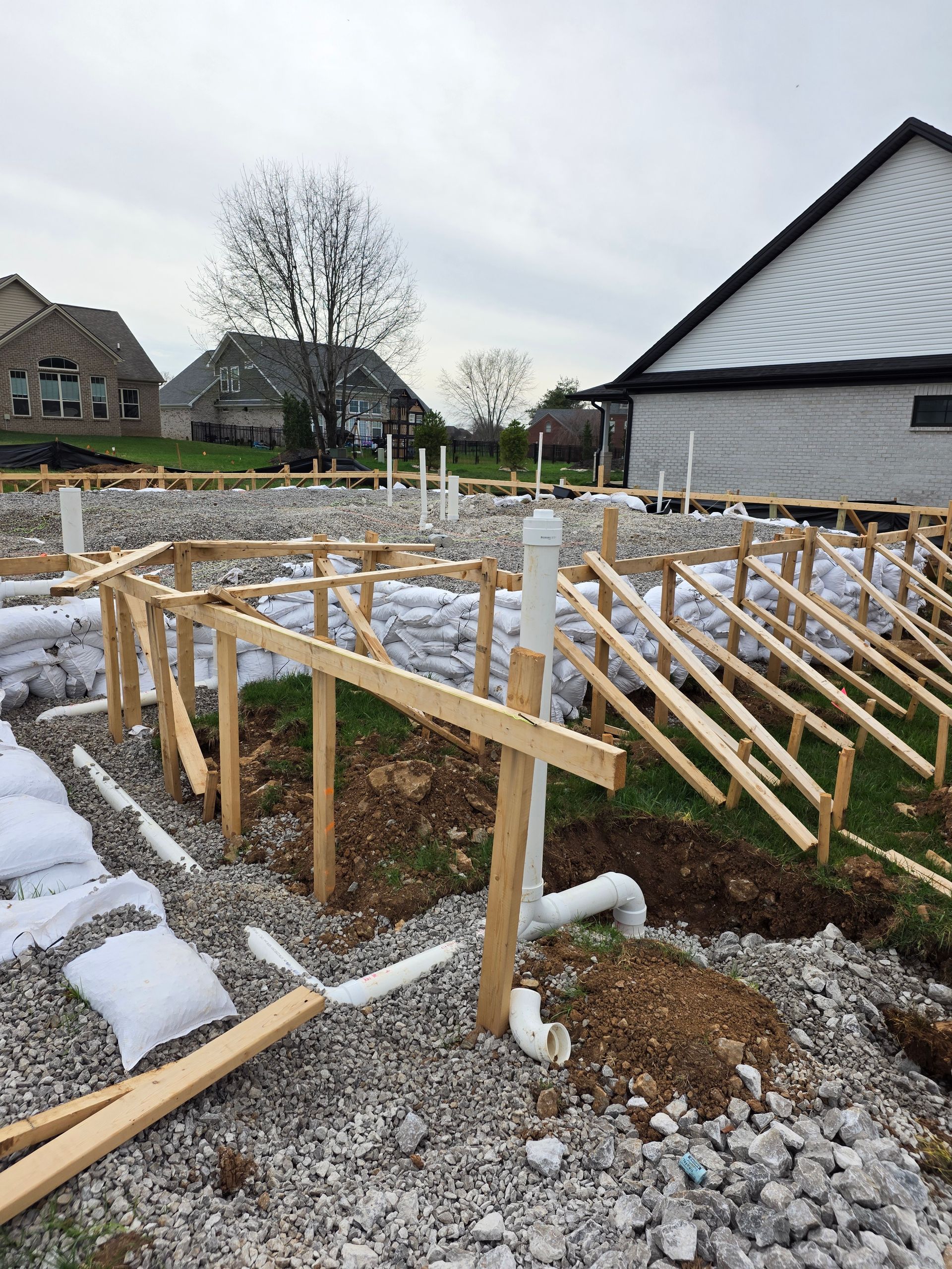 Wooden foundation framing on a snowy construction site with houses in the background