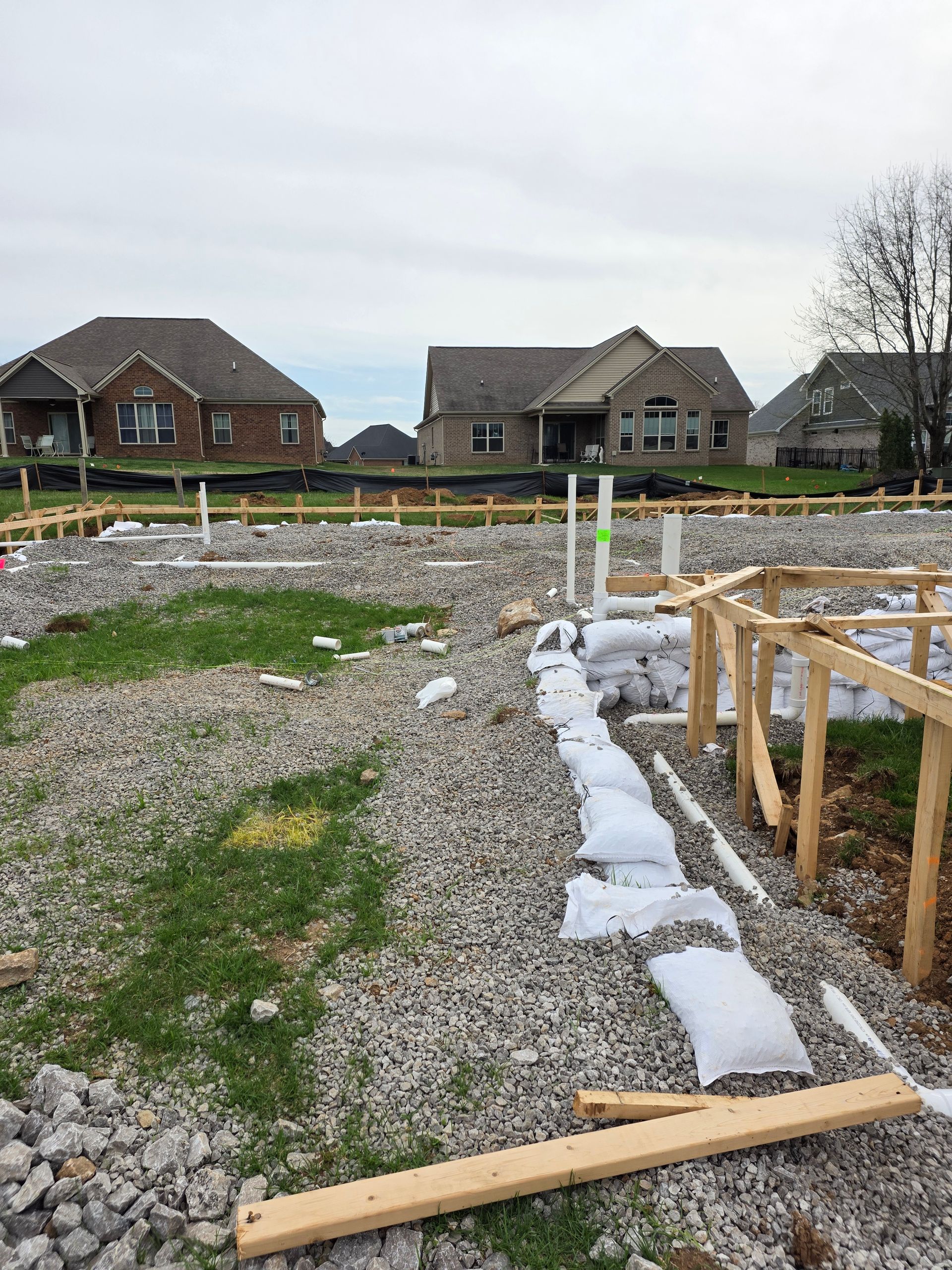 Gravel construction site with wooden forms, white wrapped materials, and houses in the background