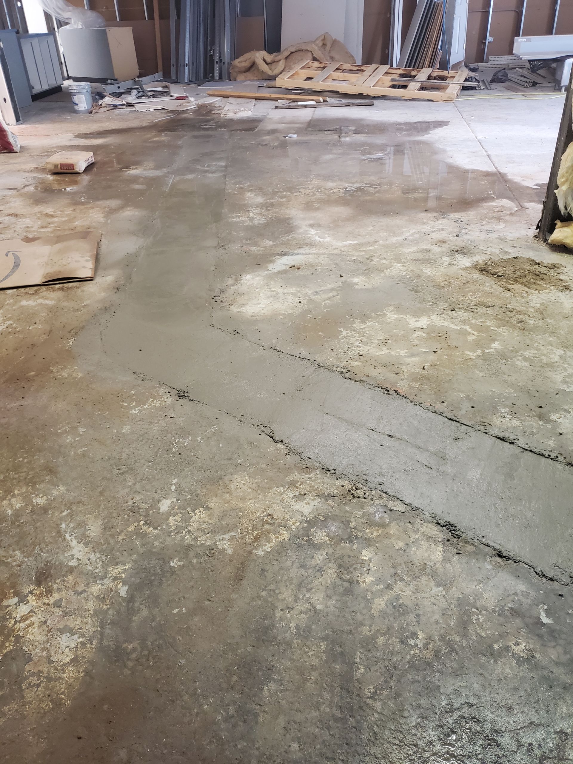 Rough concrete floor in an unfinished room with debris and construction materials along the walls.