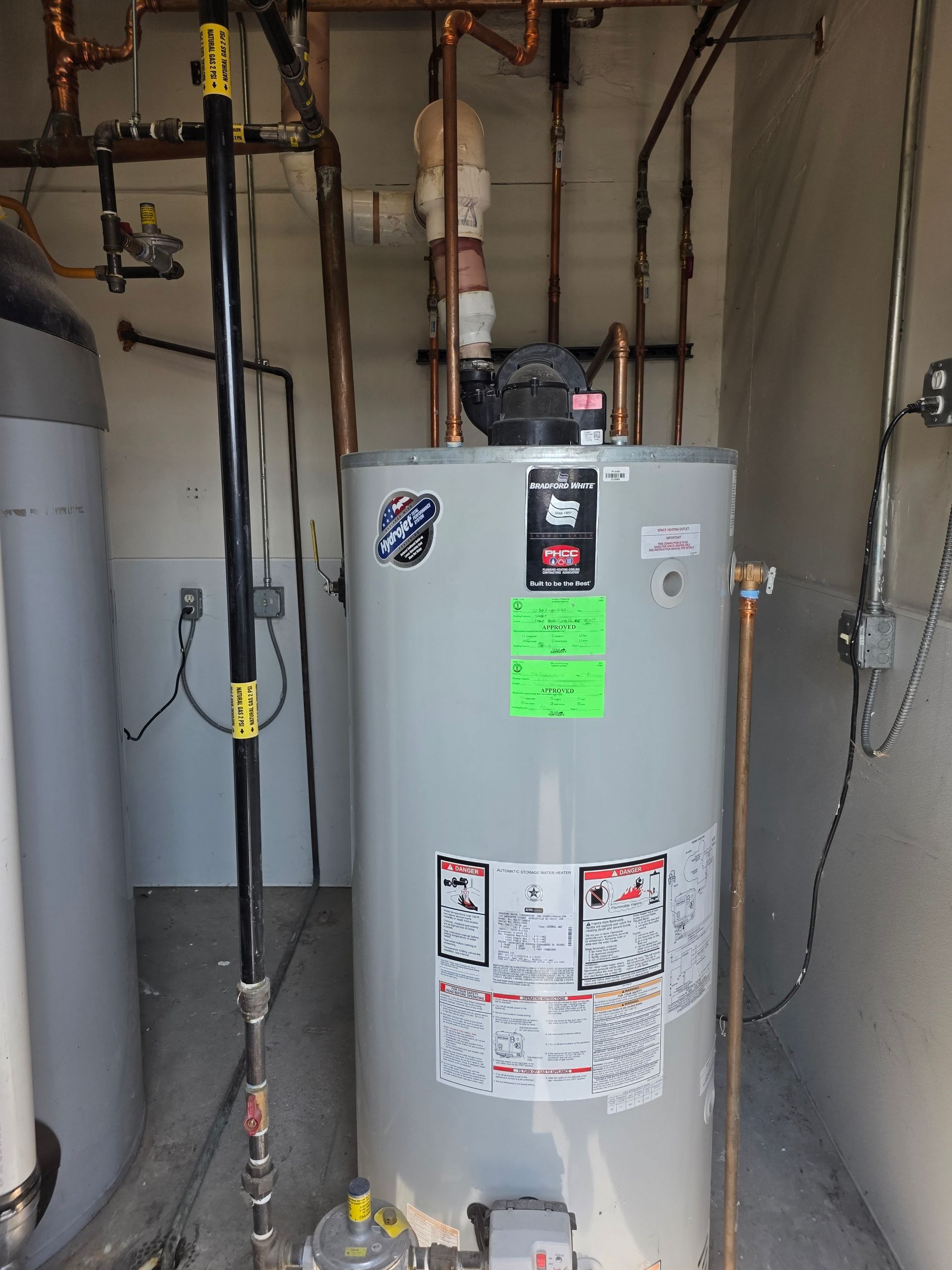 Water heater in a utility closet with exposed pipes, valves, and a sump pump tank.