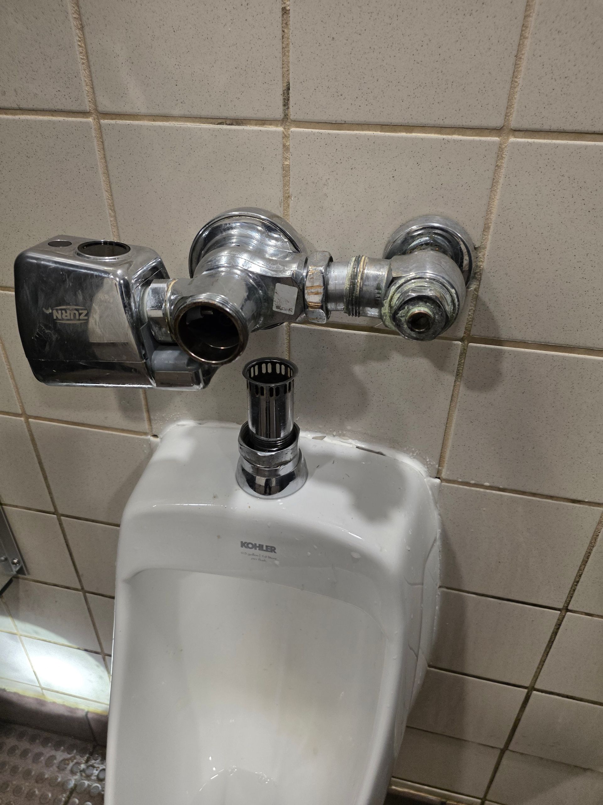 Chrome urinal flush valve and white urinal in tiled restroom