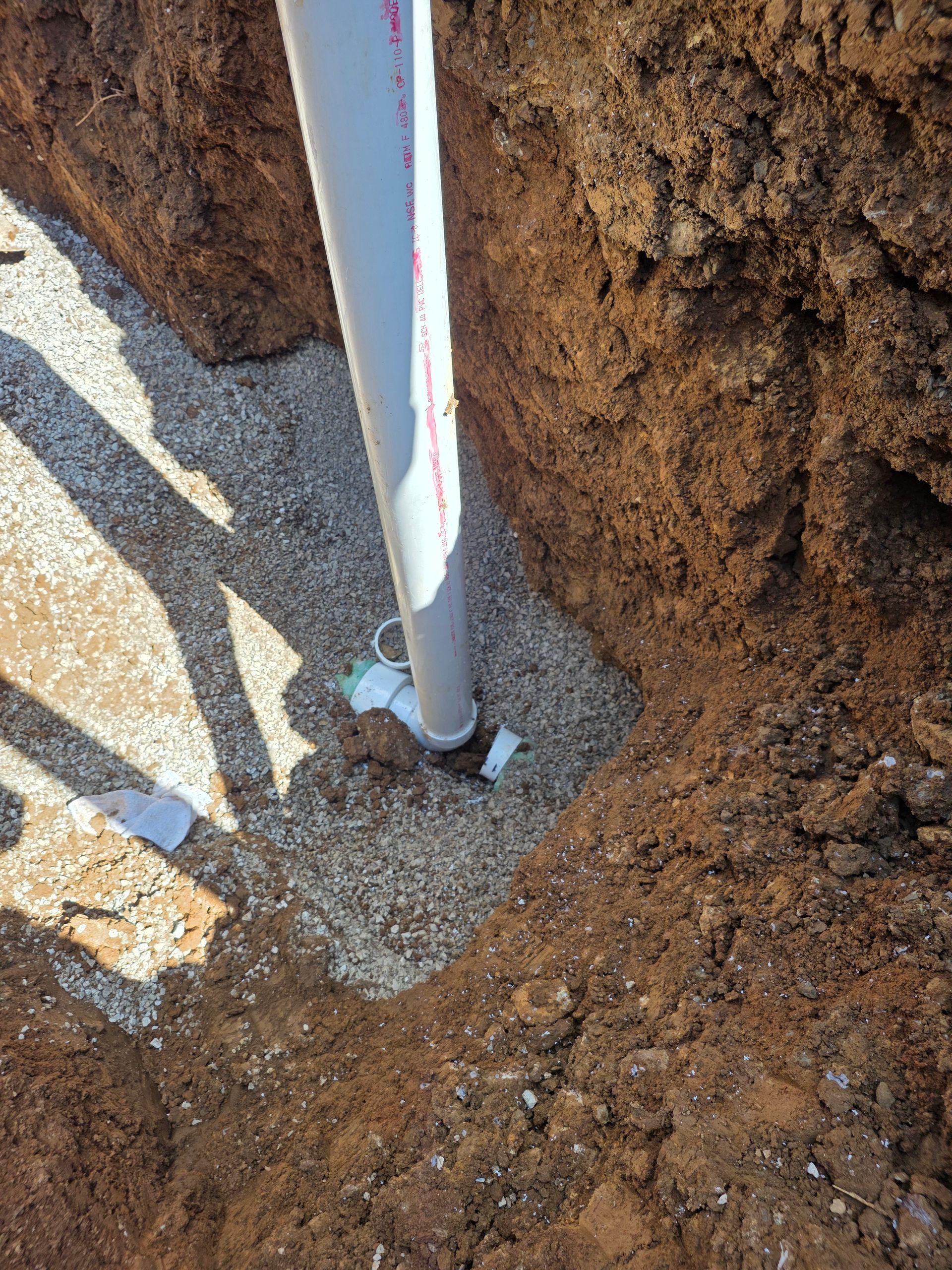 White pole in a gravel trench beside brown dirt walls, with blue tape near the base.