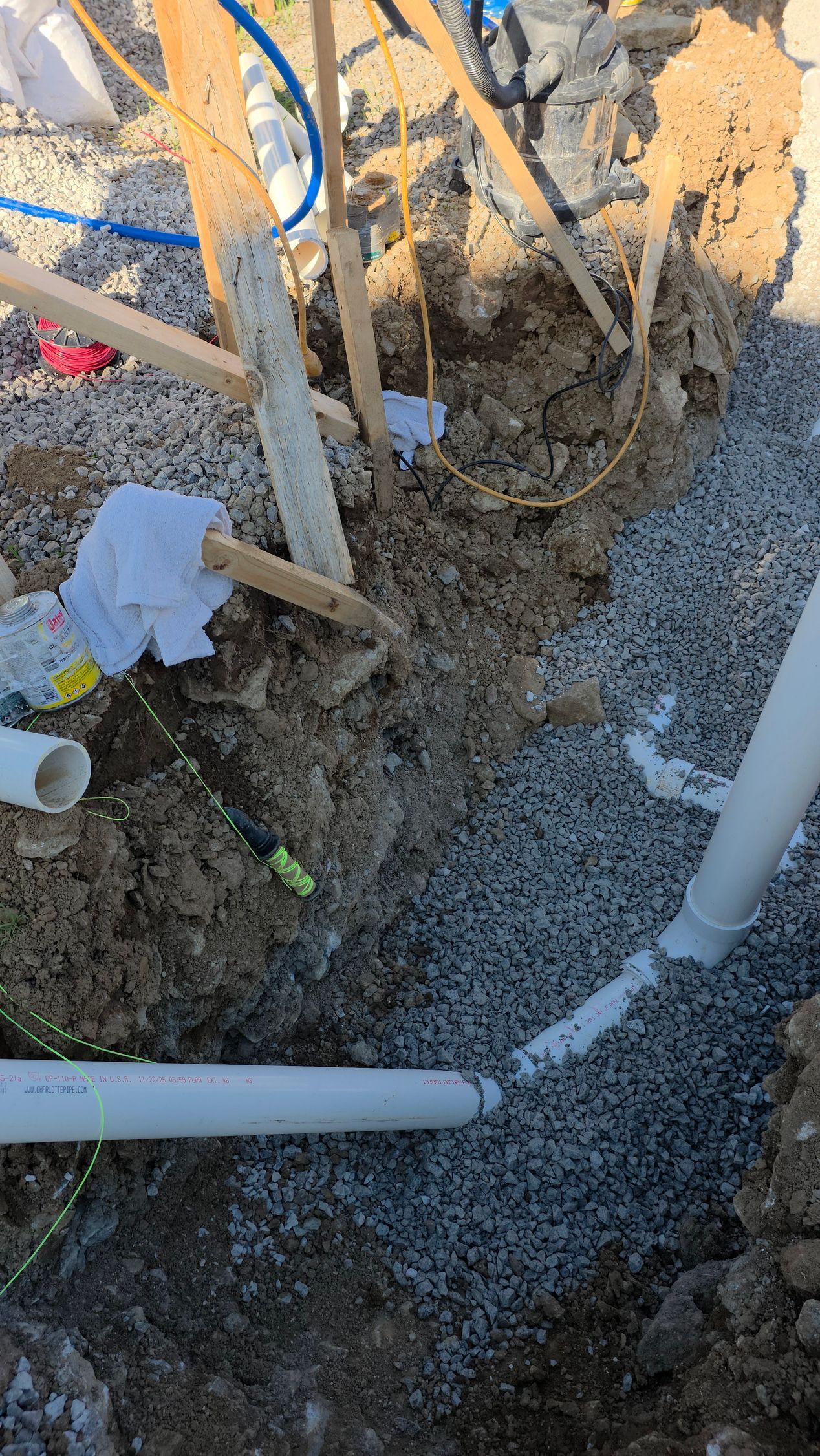 Shovel and pipes in a muddy excavation pit with exposed dirt and construction debris